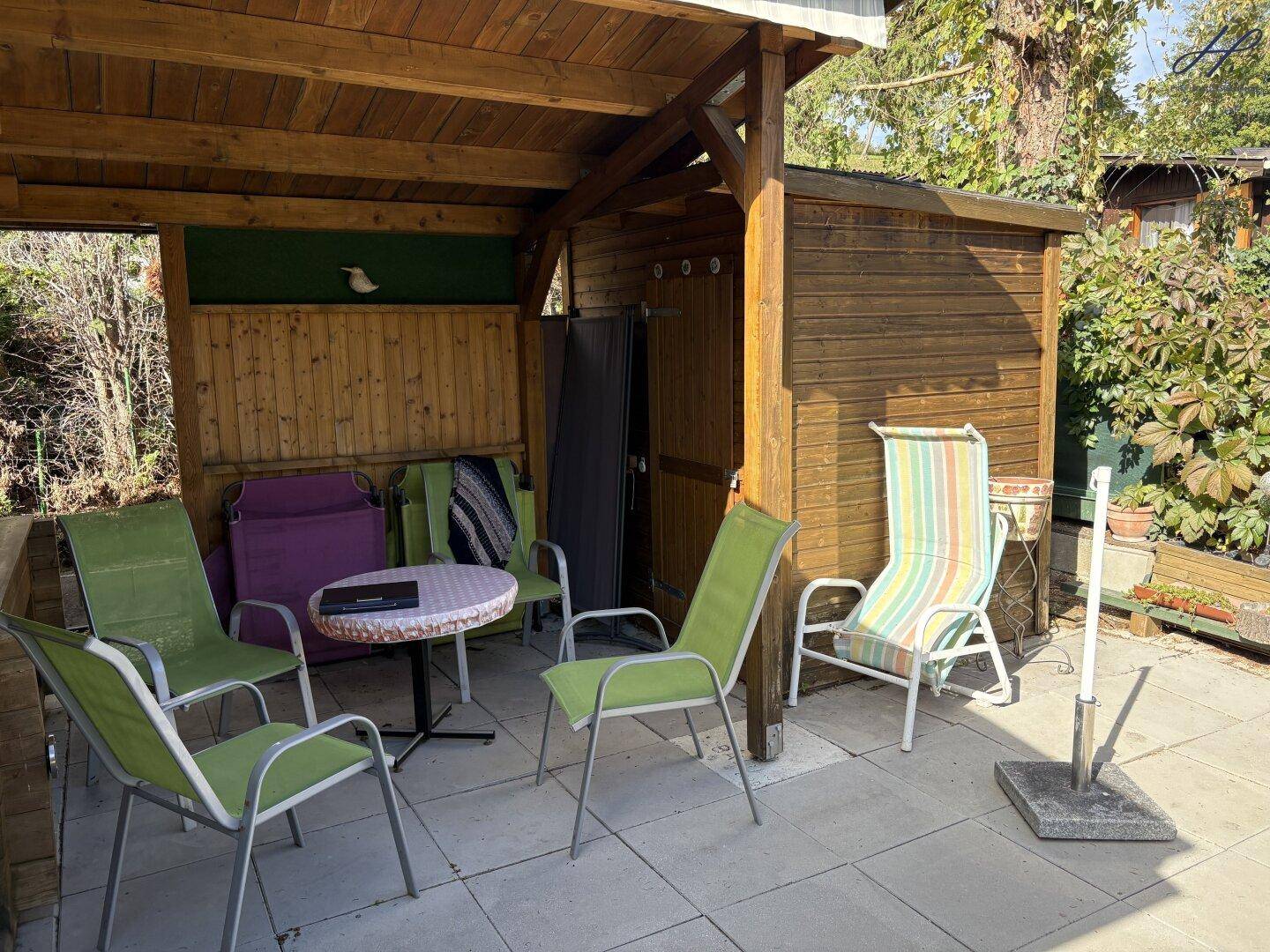 Gepflasterte Terrasse mit Gartenmöbeln und einem kleinen Holzschuppen im Grünen.
