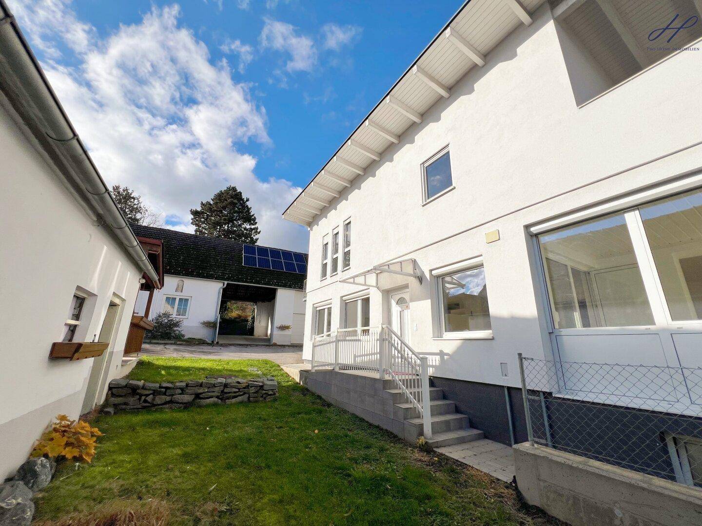 Seitenansicht des weißen Wohnhauses mit Treppe, Gartenbereich und Solarpaneelen auf dem Dach.
