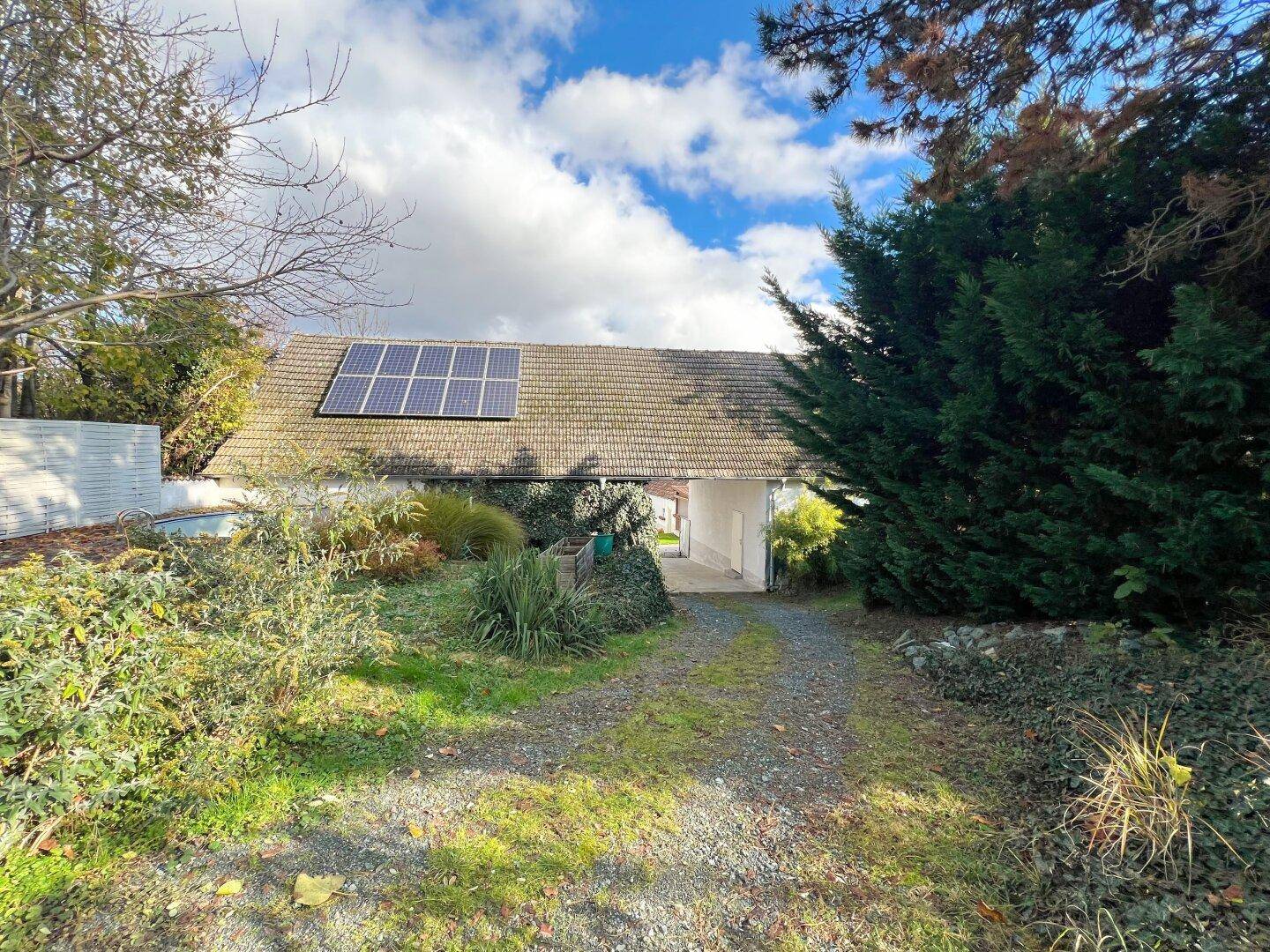 Zufahrt zum Gebäude mit üppiger Bepflanzung und Solarpaneelen auf dem Dach unter blauem Himmel.
