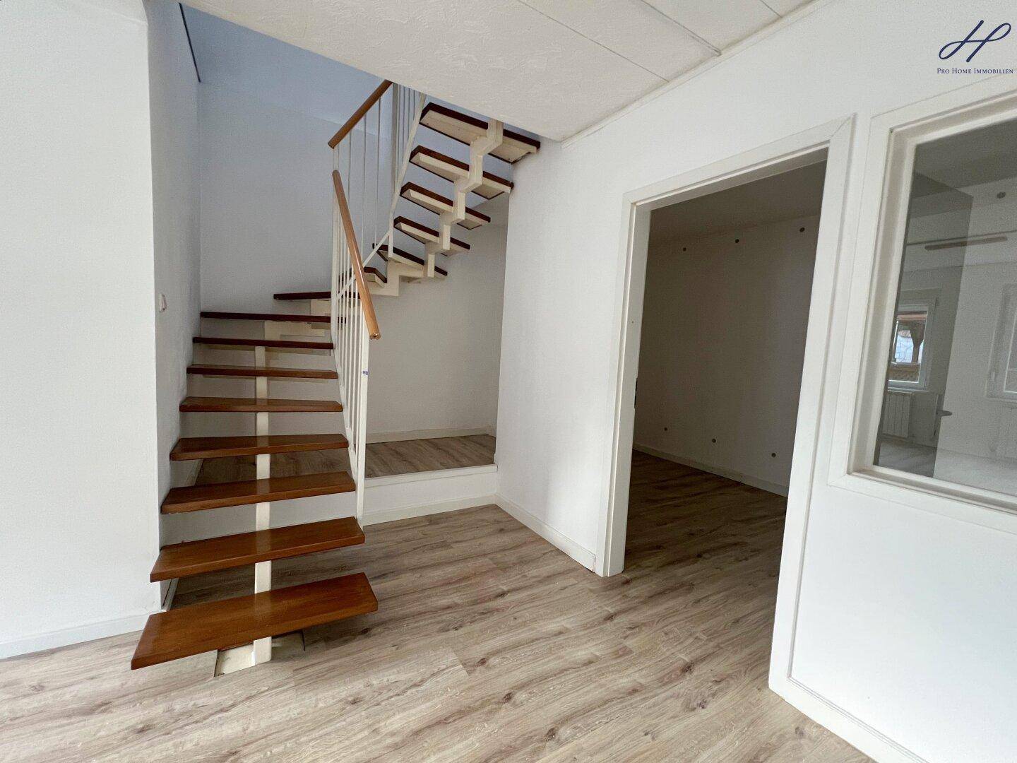 Heller Flurbereich mit offener Holztreppe und Laminatboden, der zu den oberen Etagen führt.