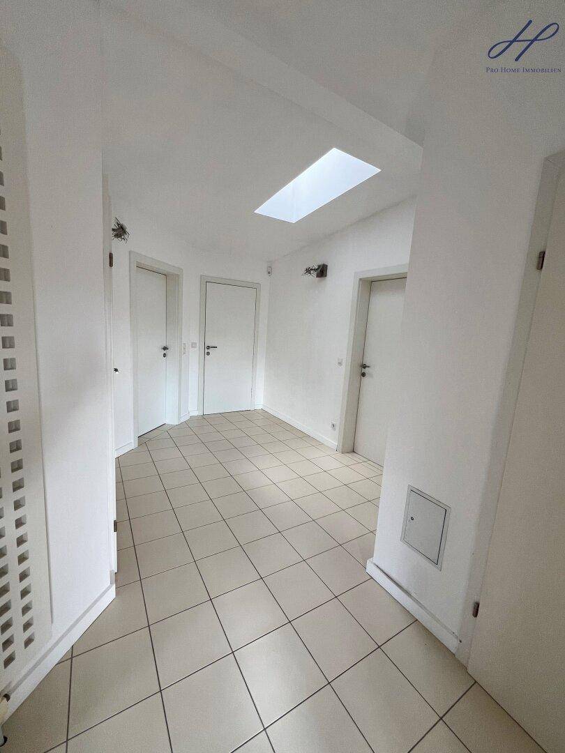 Heller Flur mit Fliesenboden, mehreren Türen und Oberlicht für natürliches Licht.