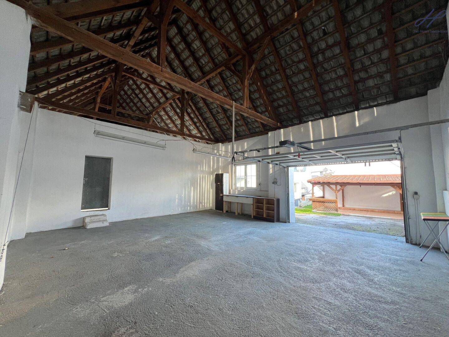 Große Garage mit Rolltor, Betonboden und sichtbaren Holzbalken im Dachbereich.