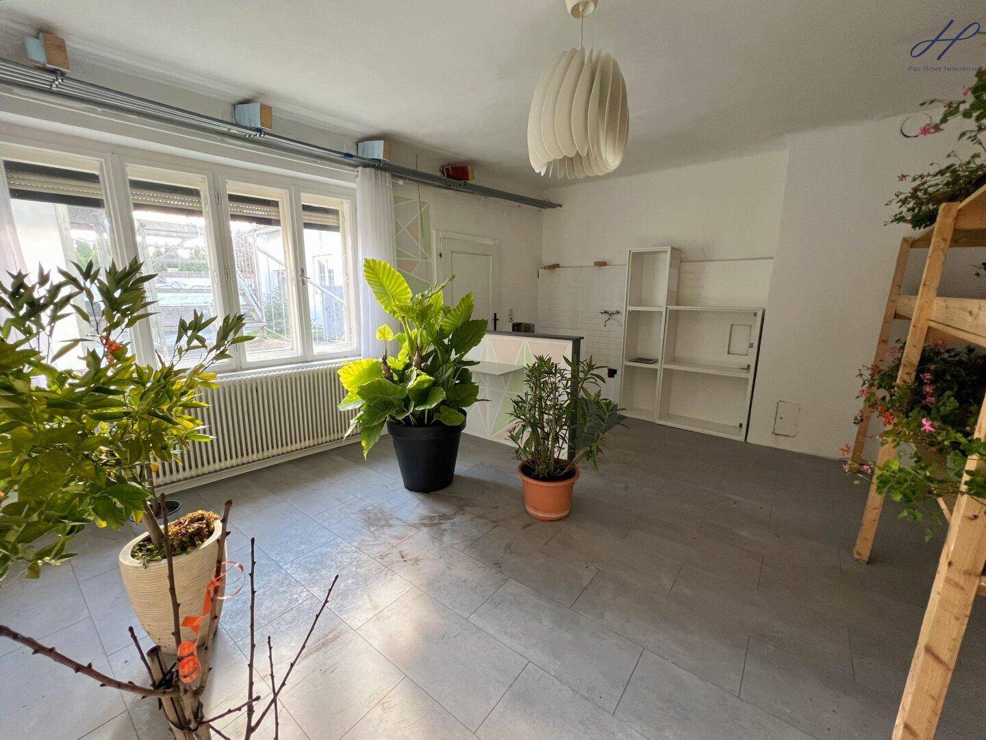 Heller Raum mit Fliesenboden, großen Fenstern und Pflanzen, vielseitig nutzbar.