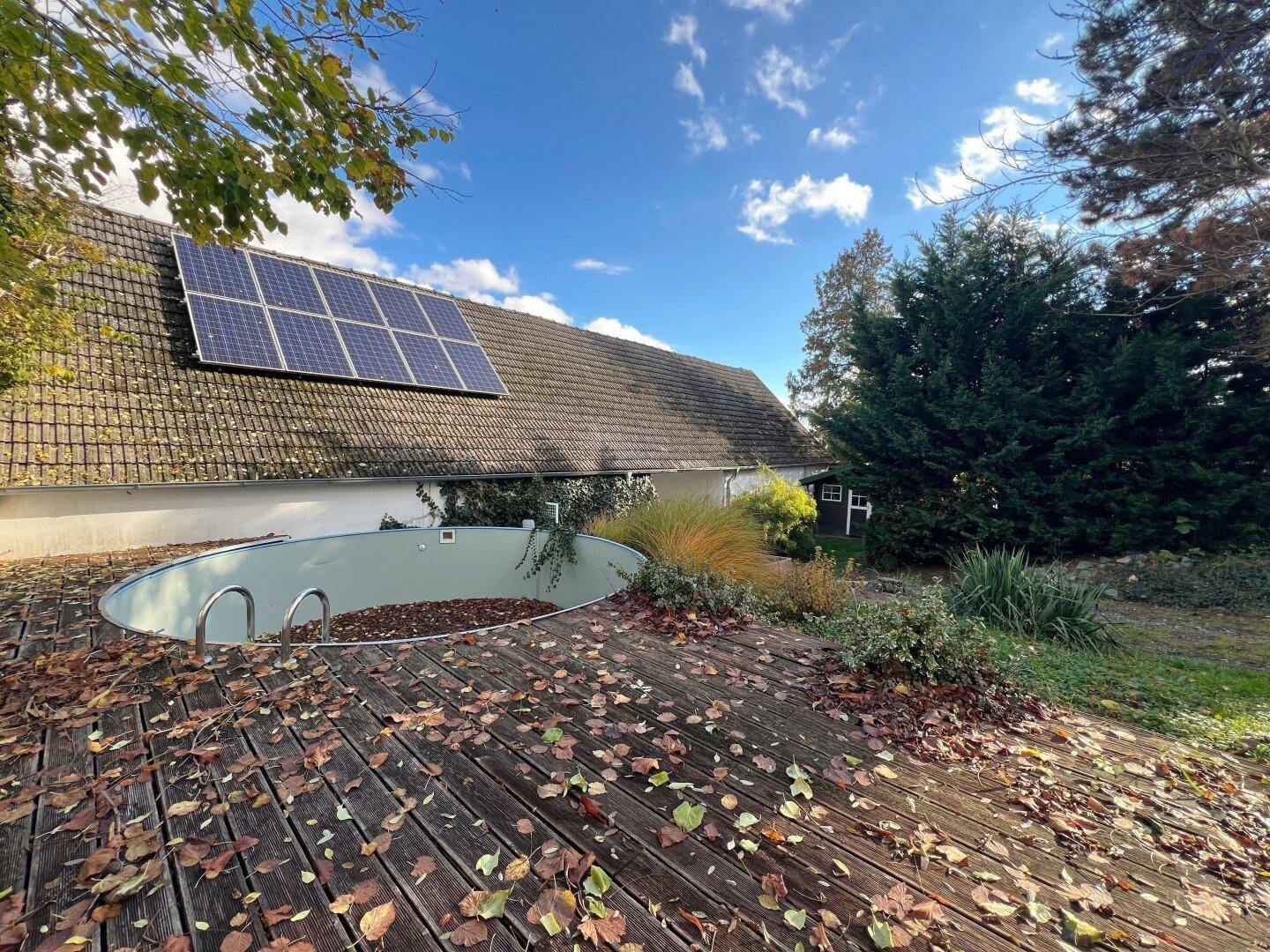 Garten mit Holzdeck, eingelassenem Pool und Solarpaneelen auf dem Dach des Hauses.