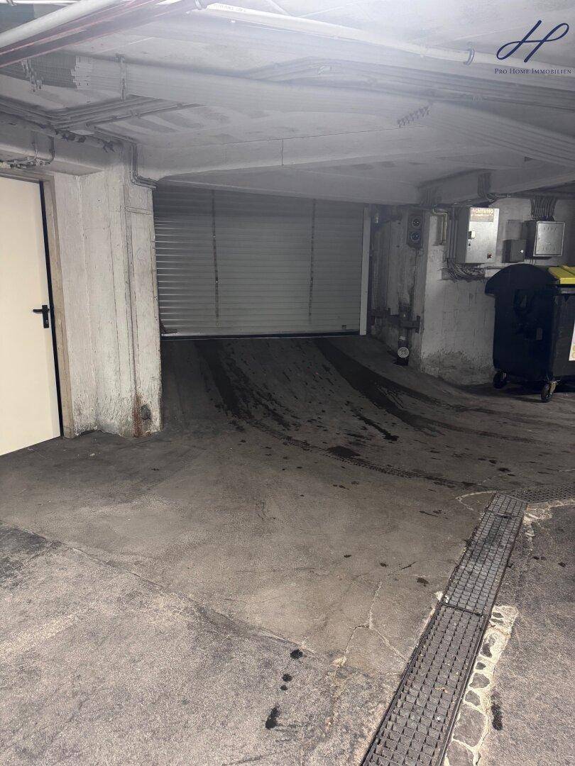 Einfahrt zur Tiefgarage mit Rolltor und Mülltonnen im Hintergrund.