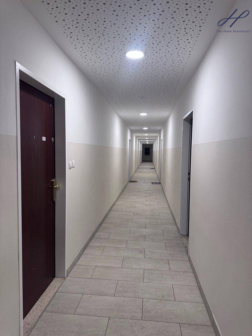 Langer, heller Flur mit Fliesenboden und vielen Türen zu den Wohneinheiten.