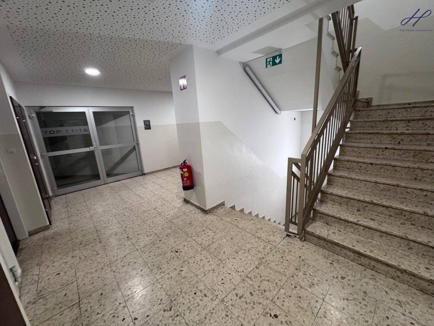 Treppenhaus mit Terrazzoboden und Metallgeländer, führt zu den oberen Etagen.