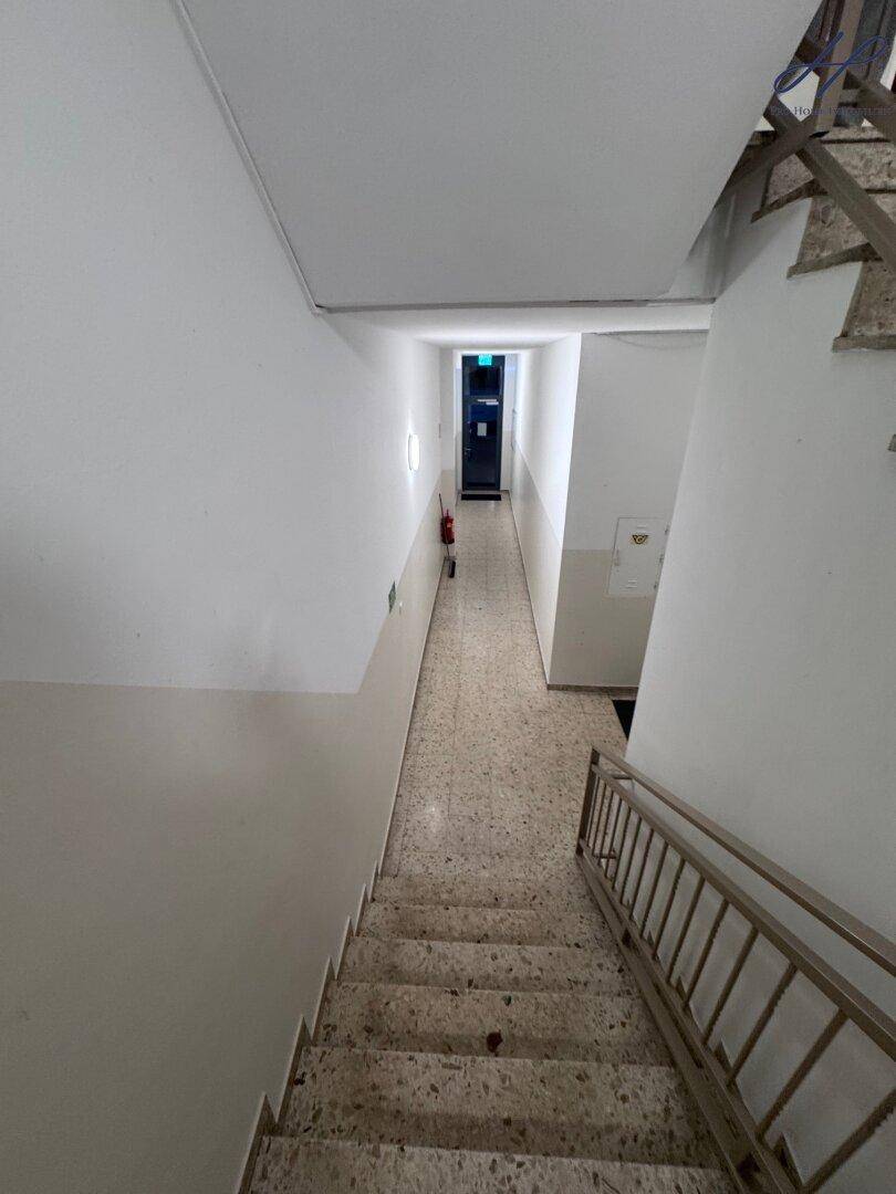 Weiterer Blick ins Treppenhaus mit Fliesenboden und Zugang zu einem langen Flur.