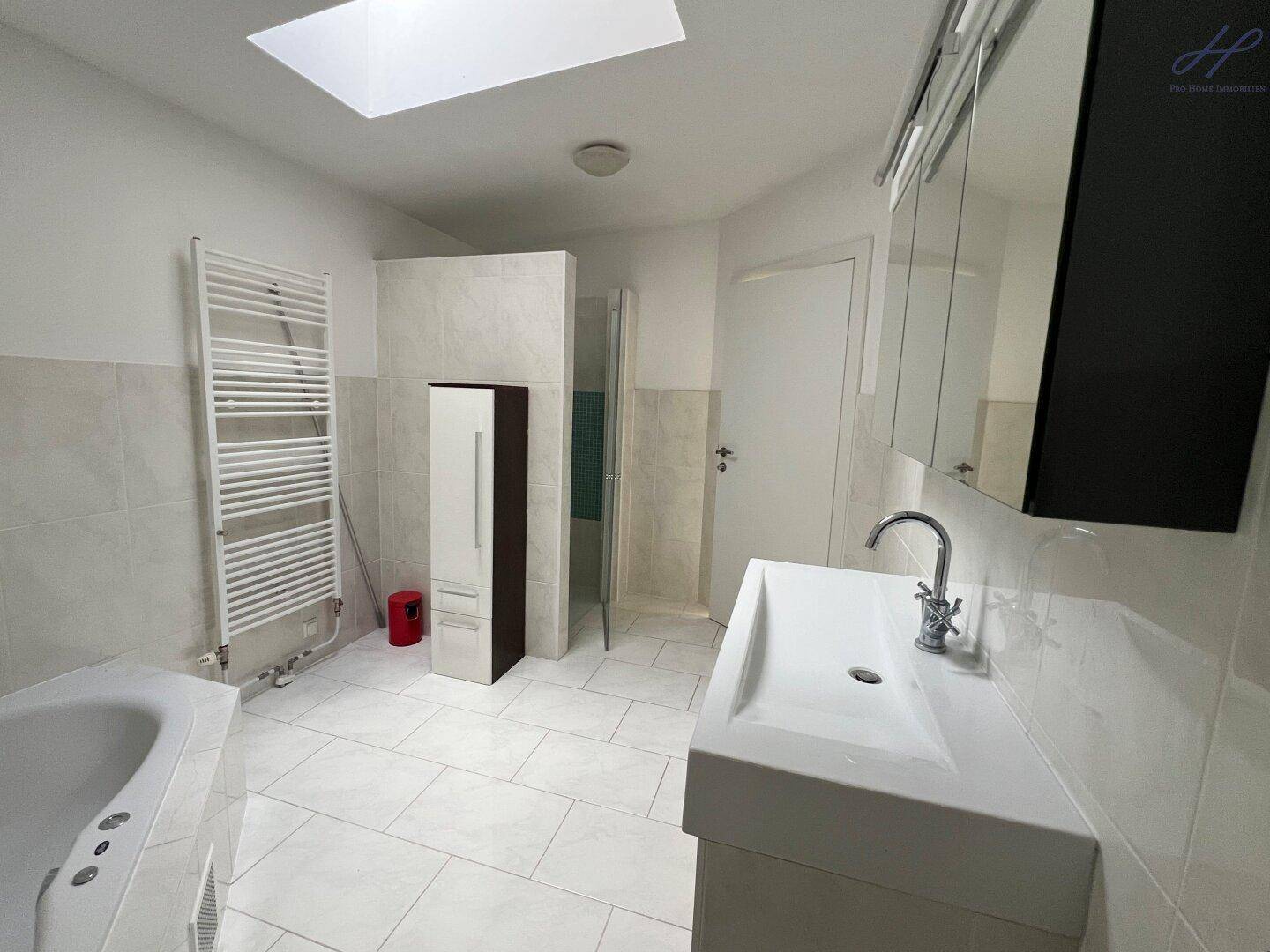 Helles Badezimmer mit Badewanne, Waschtisch, beheiztem Handtuchhalter und Oberlicht.