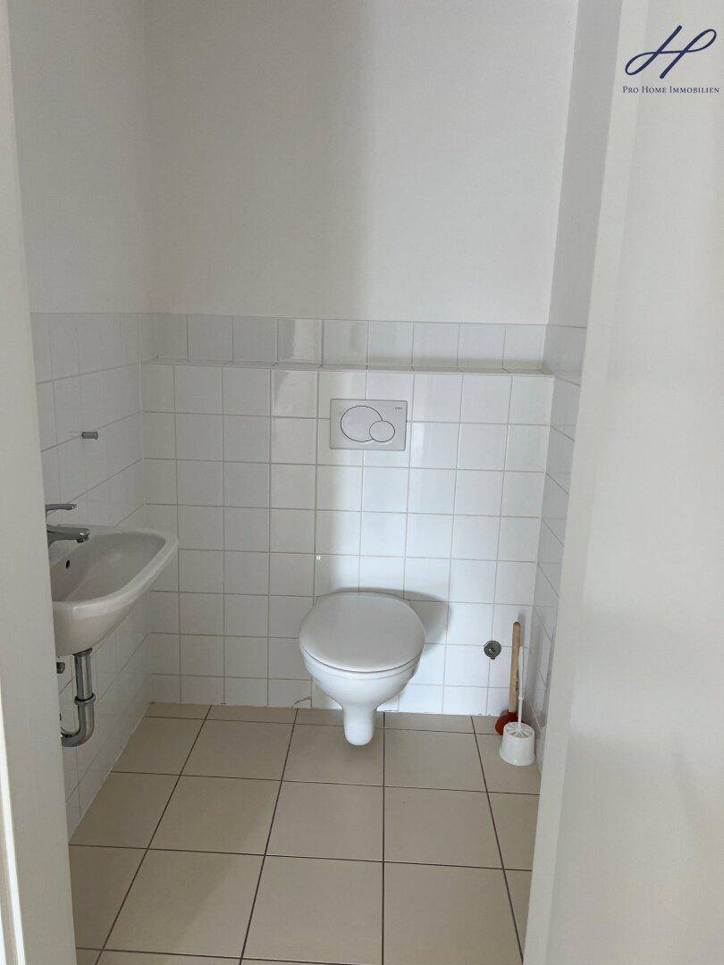Einfache Gästetoilette mit Waschbecken, WC und Fliesenboden in sauberem Zustand.