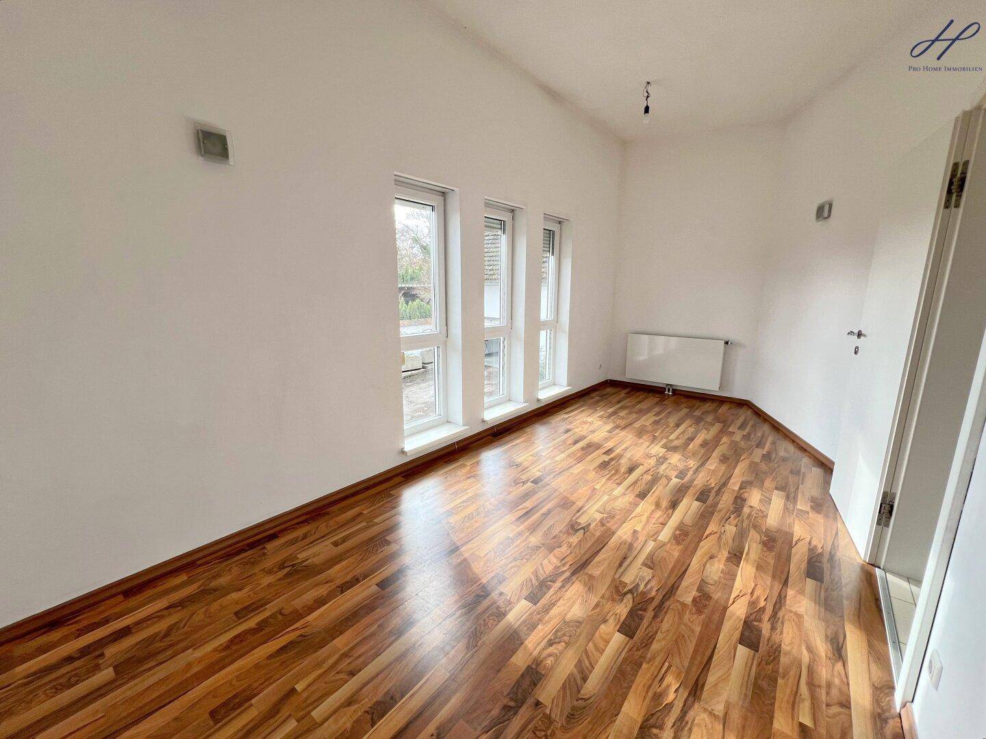 Helles, leeres Zimmer mit Holzparkettboden und mehreren Fenstern, bereit zur individuellen Gestaltung.