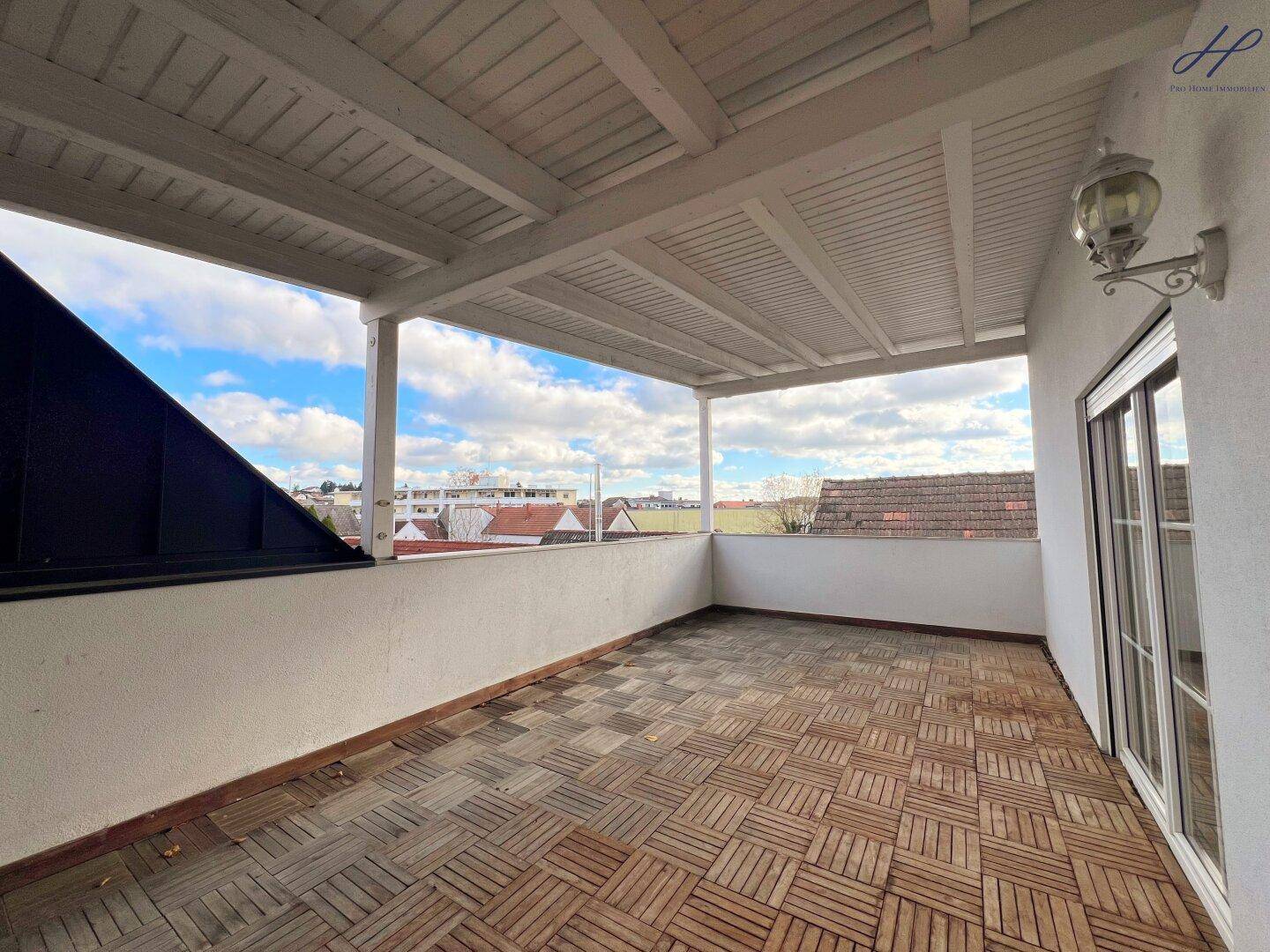 Überdachte Terrasse mit Holzbodenfliesen und weitem Blick über die Umgebung.