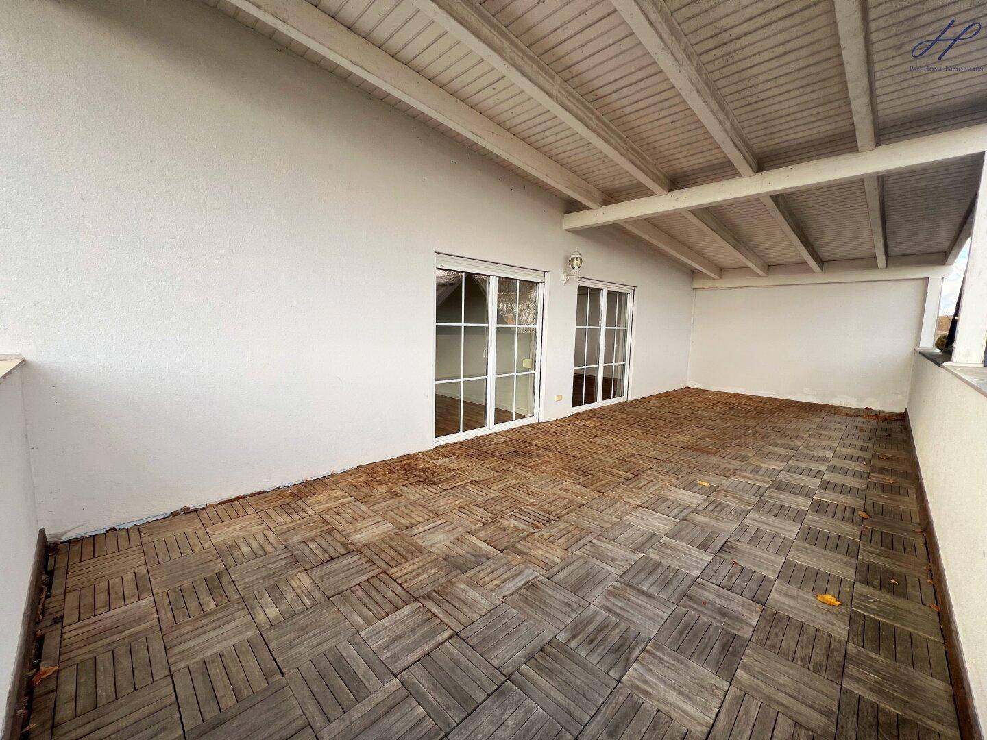 Geräumige überdachte Terrasse mit Holzboden und Zugang zu den Innenräumen durch große Türen.
