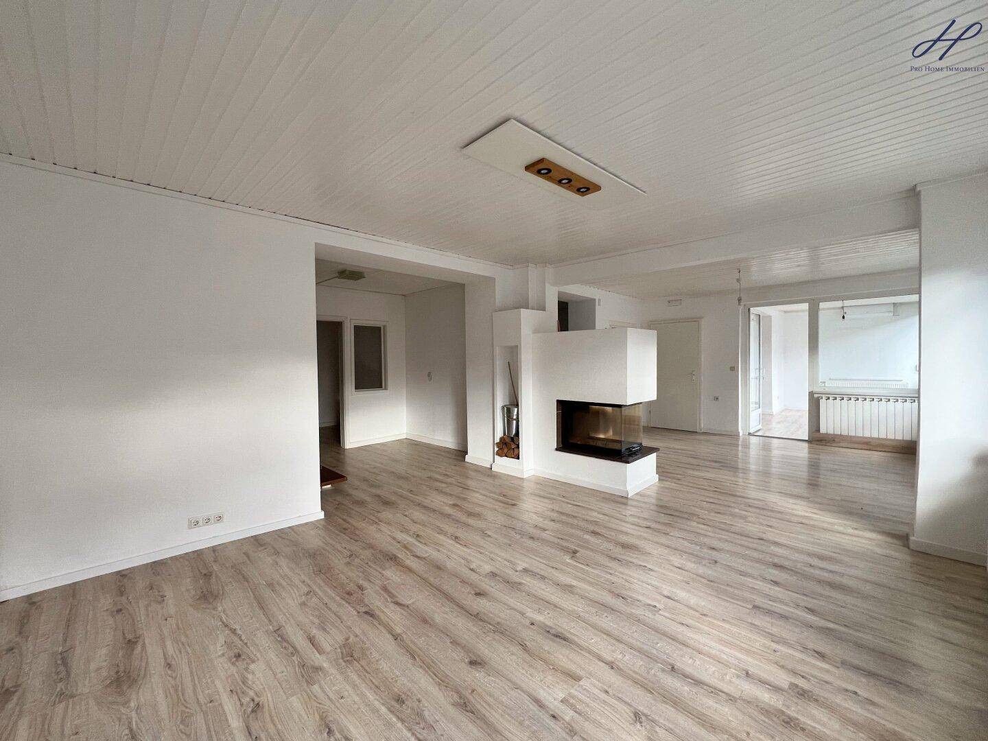 Geräumiges Wohnzimmer mit modernem Kamin als Raumteiler und hellem Laminatboden.
