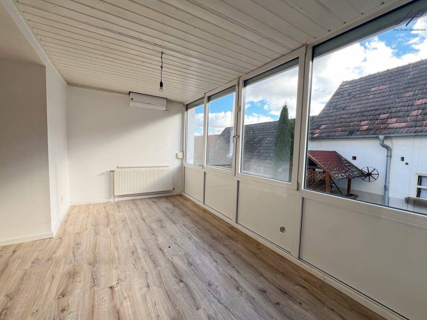Heller Wintergarten mit großen Fenstern, Laminatboden und Klimaanlage, ideal zum Entspannen.
