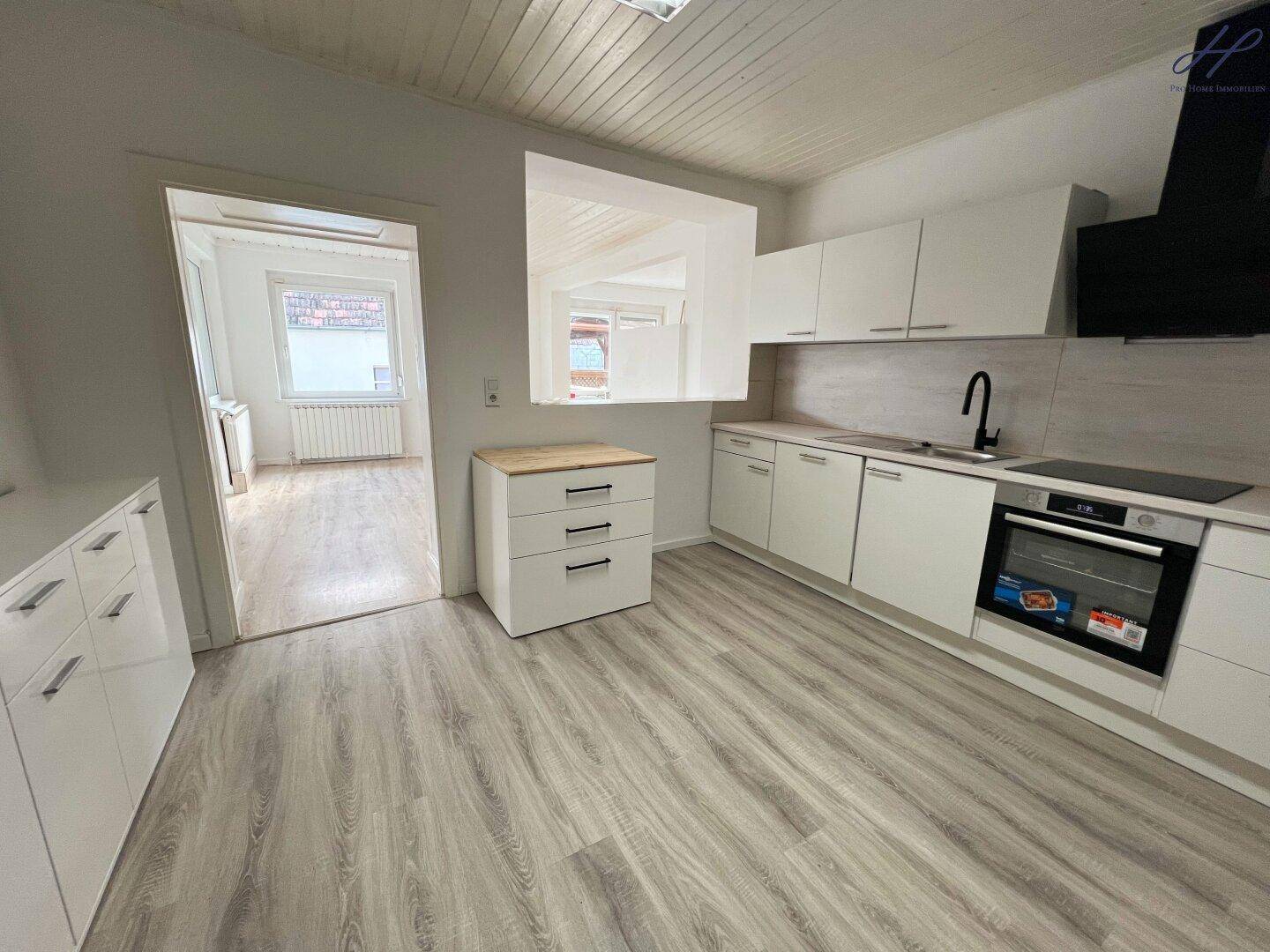 Moderne Küche mit weißen Schränken, Holzarbeitsplatte, Laminatboden und integrierten Geräten.