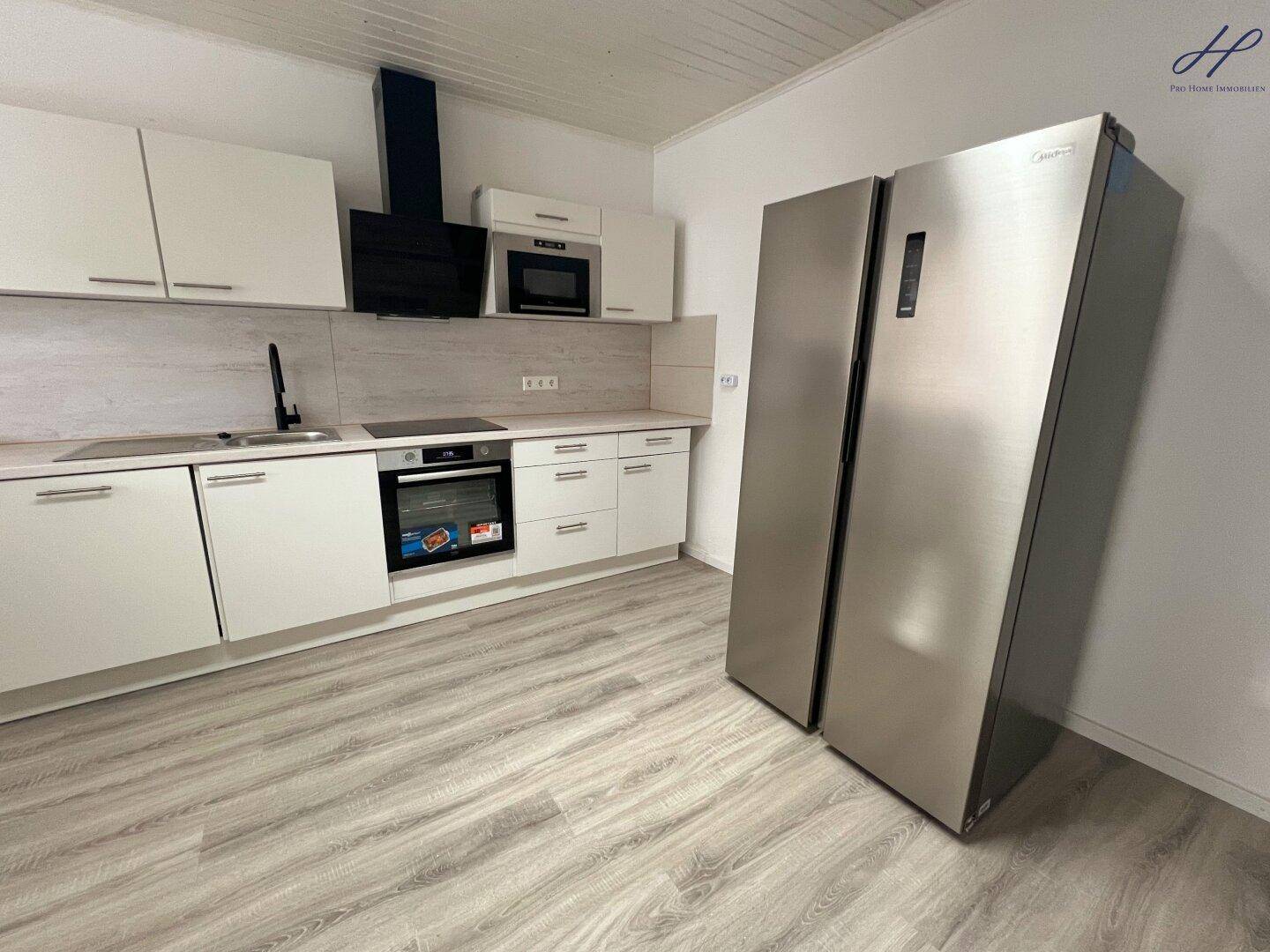 Neue Küche mit weißen Fronten, integrierten Geräten und großem Edelstahl-Kühlschrank.