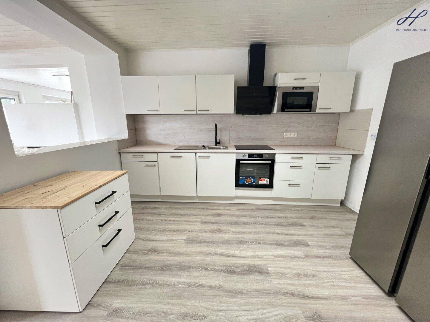 Helle Einbauküche mit weißen Schränken, Holzdetails und modernen Geräten, bereit zum Kochen.