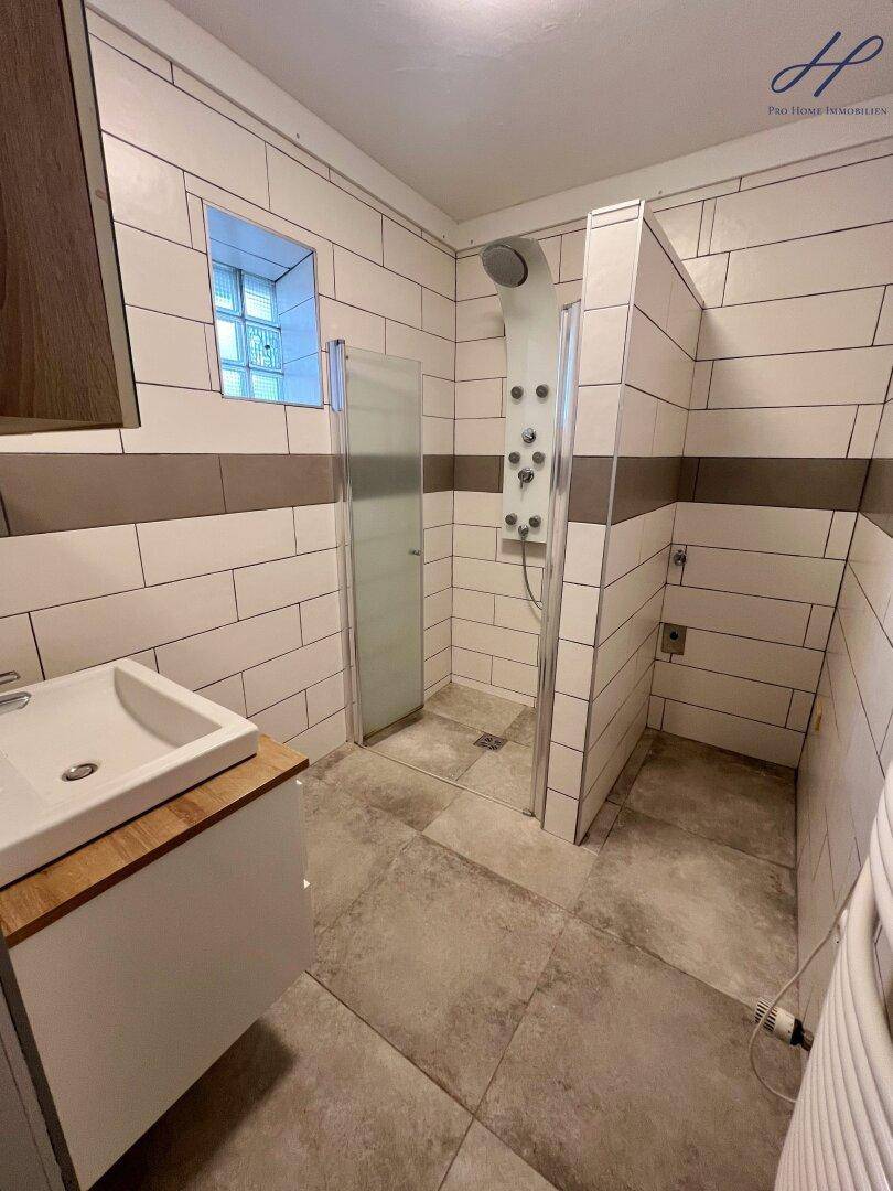 Modernes Badezimmer mit begehbarer Dusche, Fliesenboden und kleinem Fenster für Tageslicht.