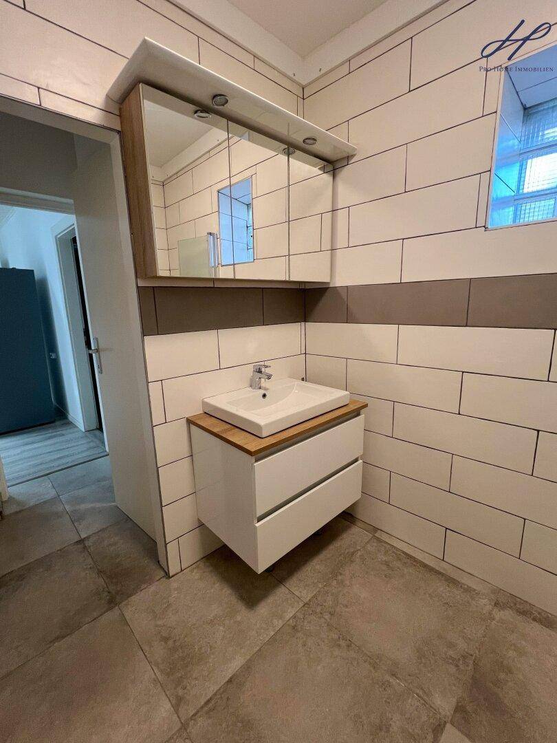 Badezimmer mit modernem Waschtisch, Spiegelschrank und gefliesten Wänden in neutralen Farben.