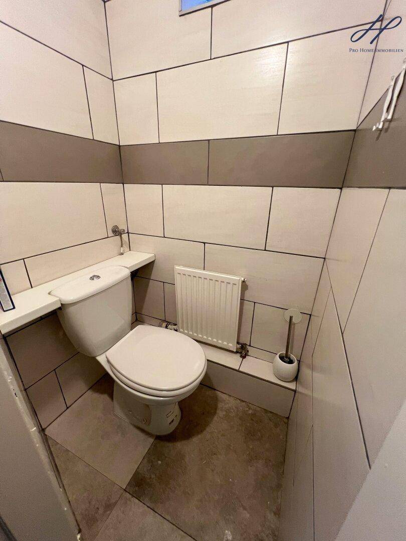 Separate Gästetoilette mit Wand-WC und Fliesen an Wänden und Boden in schlichtem Design.