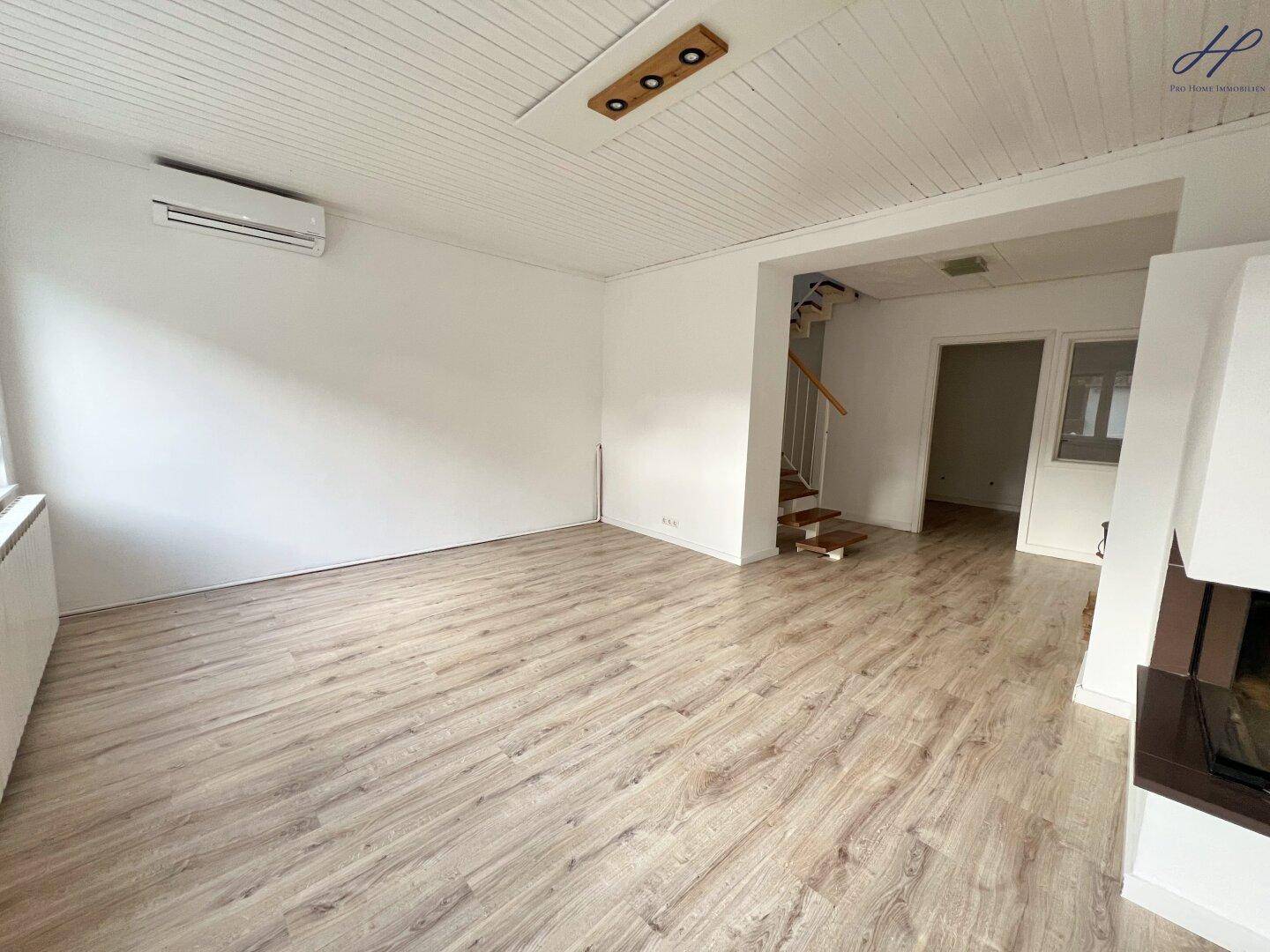 Geräumiger Wohnbereich mit Laminatboden, Kamin und offenem Zugang zur Holztreppe.