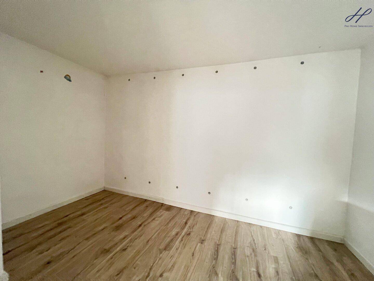 Leeres Zimmer mit hellem Laminatboden und weißen Wänden, bereit zur individuellen Gestaltung.
