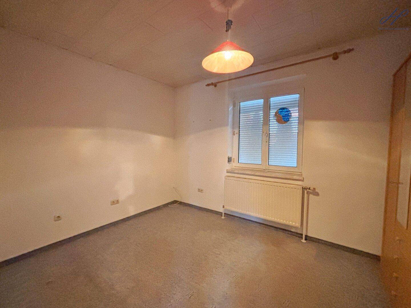 Schlafzimmer mit Teppichboden, Fenster mit Rollladen und Heizkörper.