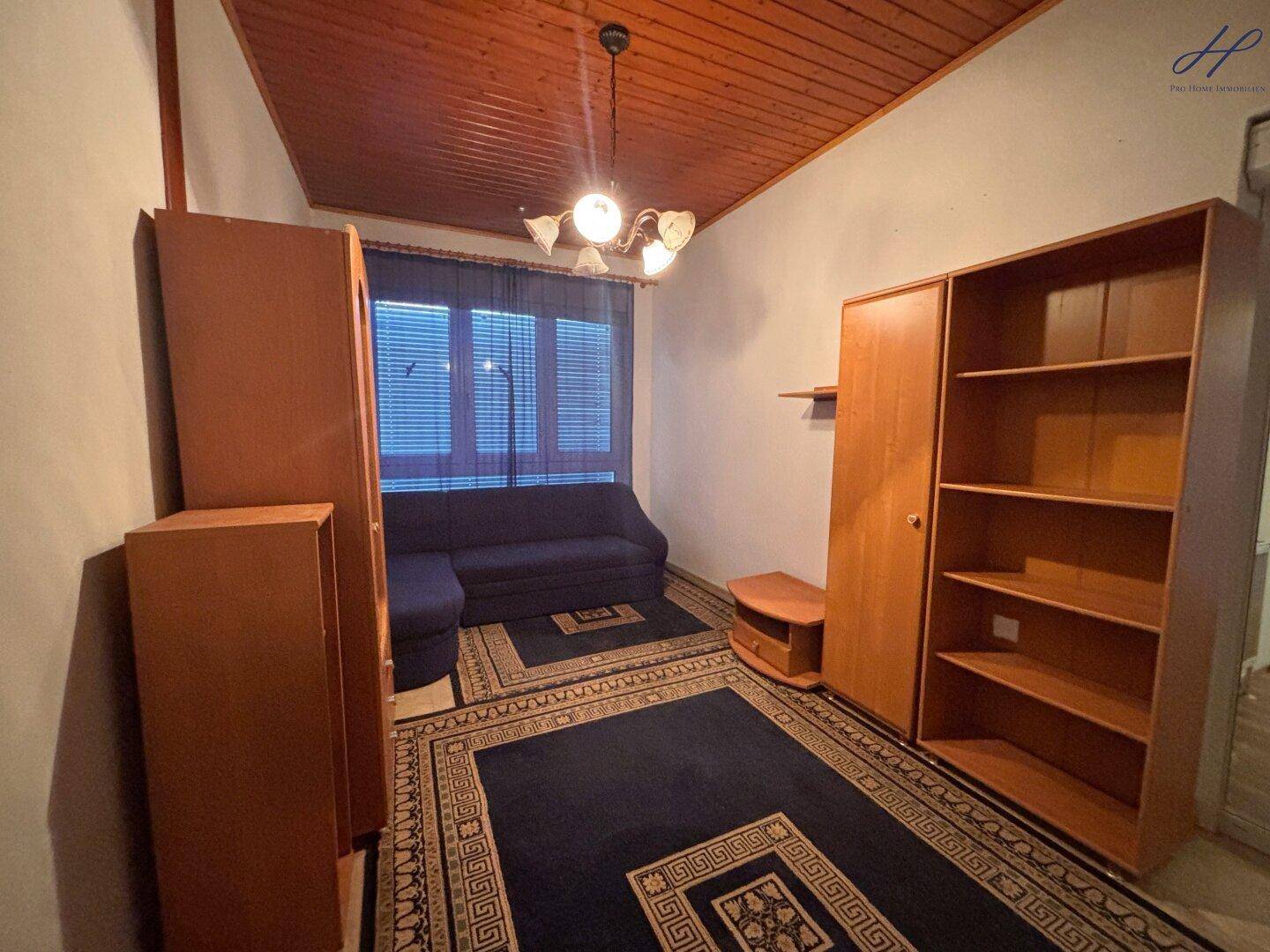Gemütliches Zimmer mit Holzdecke, Teppichboden und dunklem Sofa.