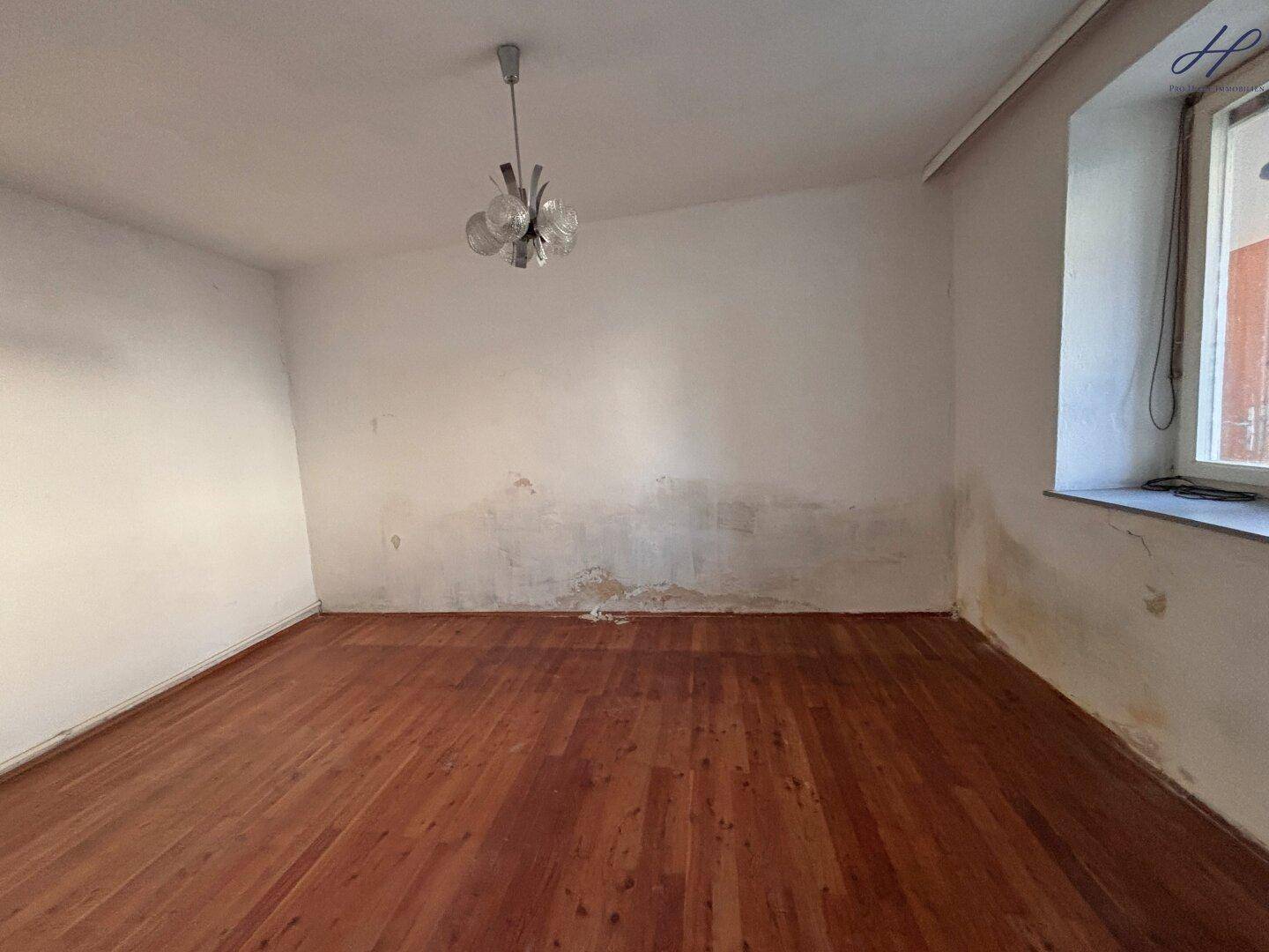 Heller Raum mit Holzboden und sichtbaren Gebrauchsspuren, renovierungsbedürftig.