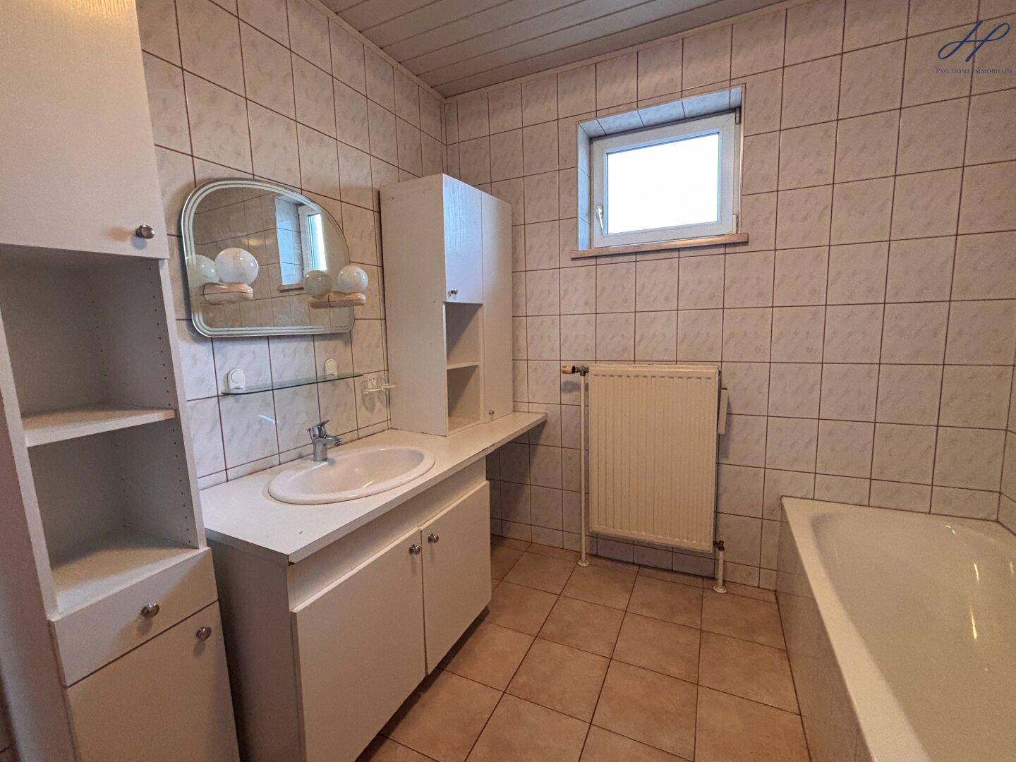 Gefliestes Badezimmer mit Waschbecken, Spiegelschrank und Badewanne.