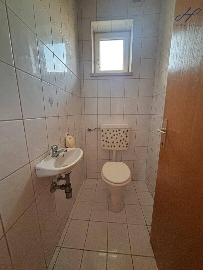 Kleines Gäste-WC mit Fenster, Waschbecken und Toilette, komplett gefliest.