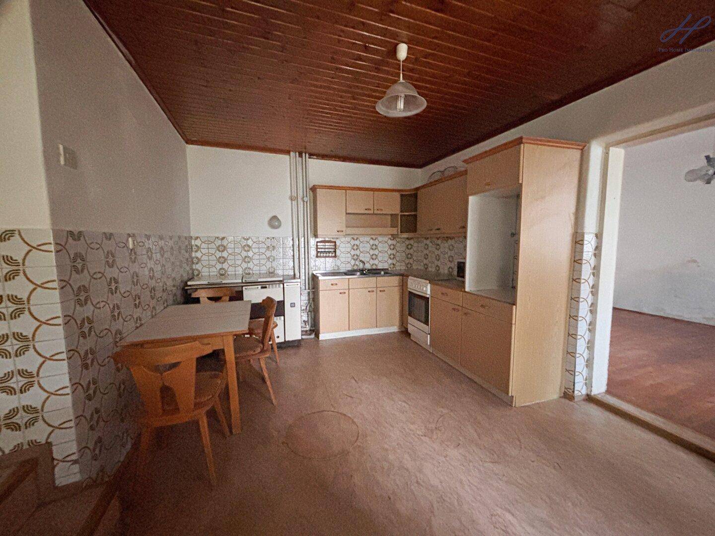 Ältere Küche mit Holzschränken, Essbereich und Holzdecke, renovierungsbedürftig.
