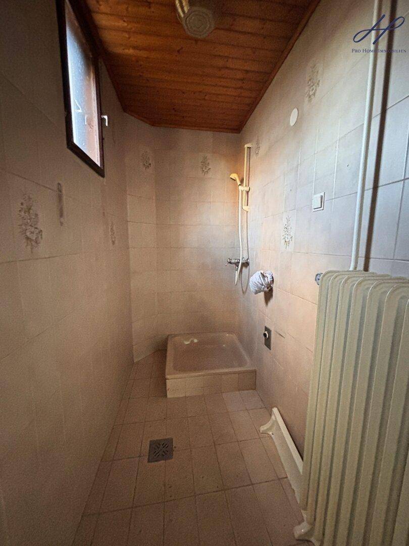 Einfacher Duschraum mit Fliesenwänden und Holzdecke, renovierungsbedürftig.