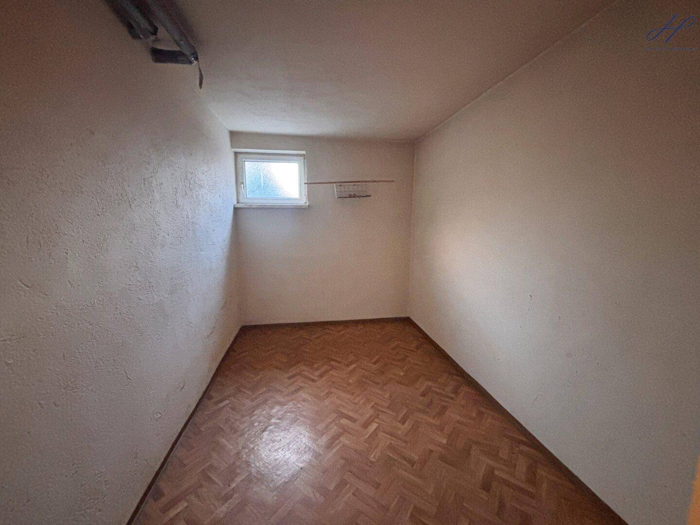 Kleiner Raum im Untergeschoss mit Parkettboden und Fenster.