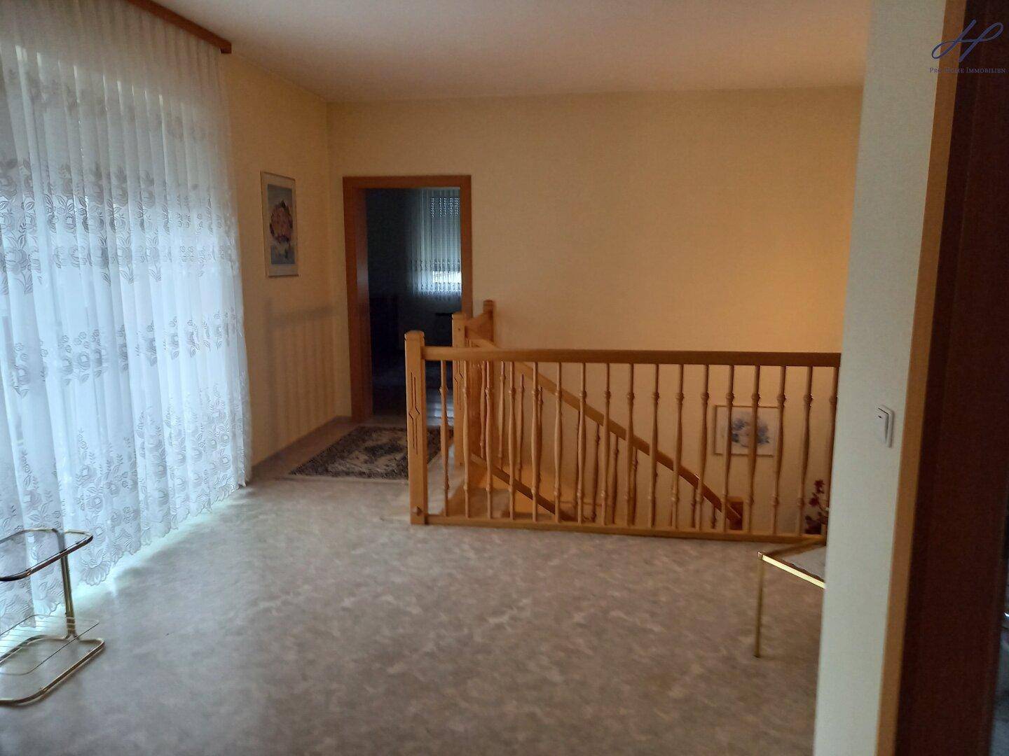 Heller Flur im Obergeschoss mit Holzgeländer und großen Fenstern.