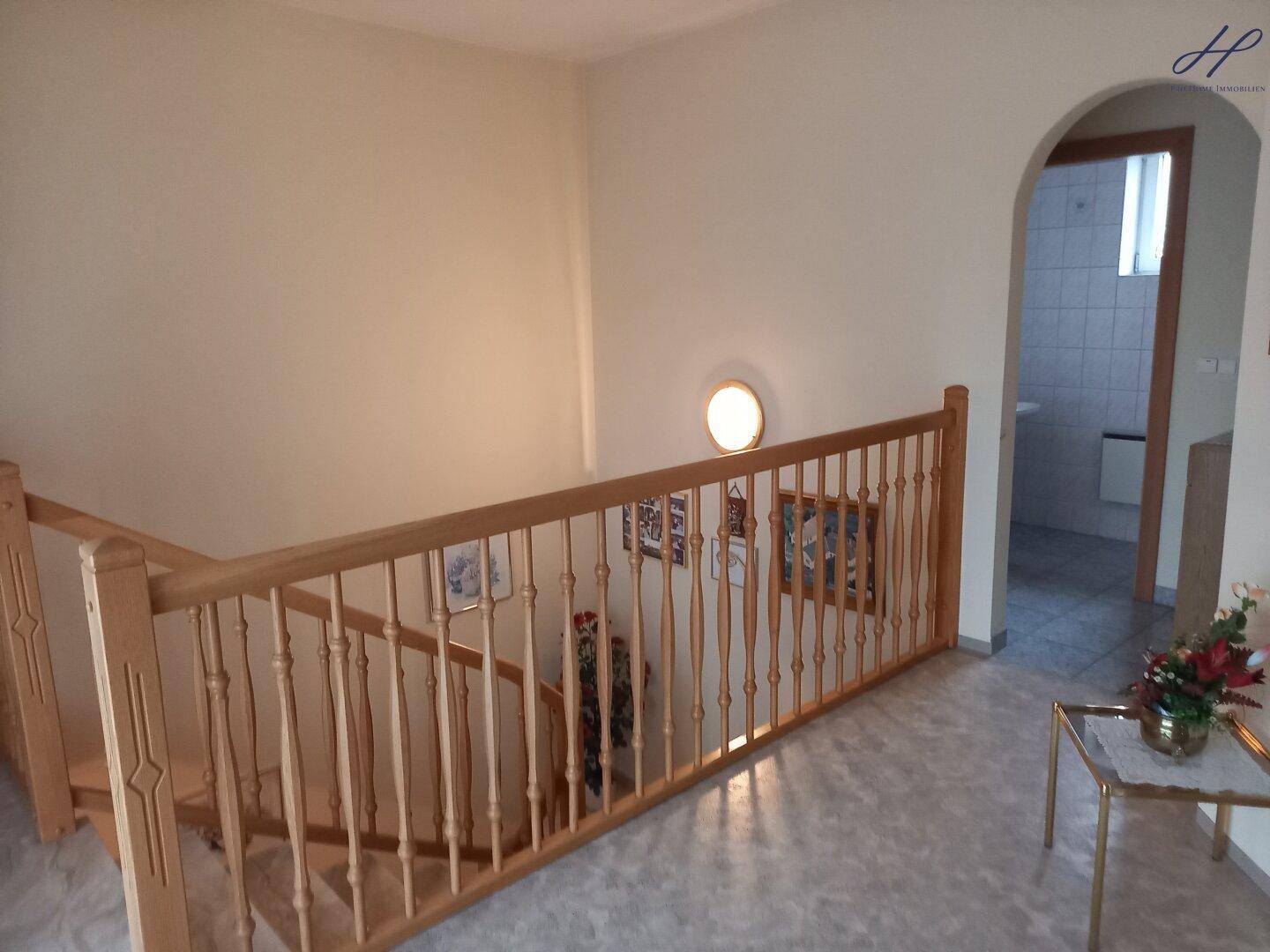 Heller Treppenaufgang mit Holzgeländer und Zugang zu weiteren Räumen.