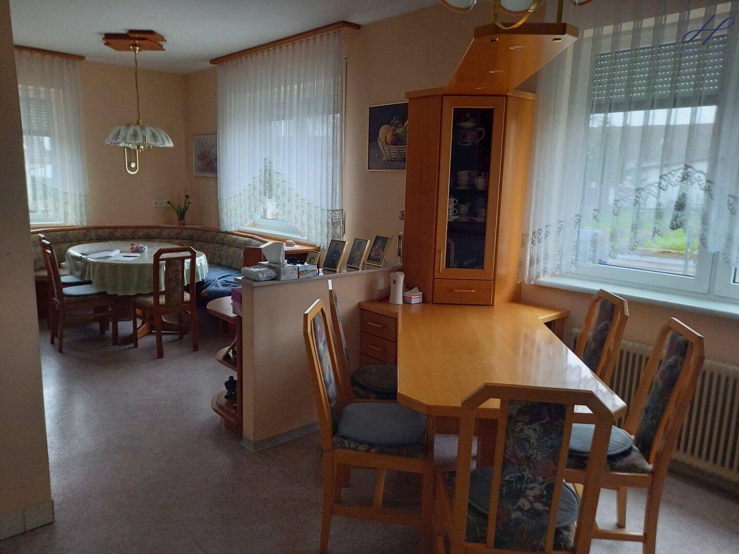 Heller Essbereich mit Eckbank, Holztisch und großen Fenstern mit Vorhängen.