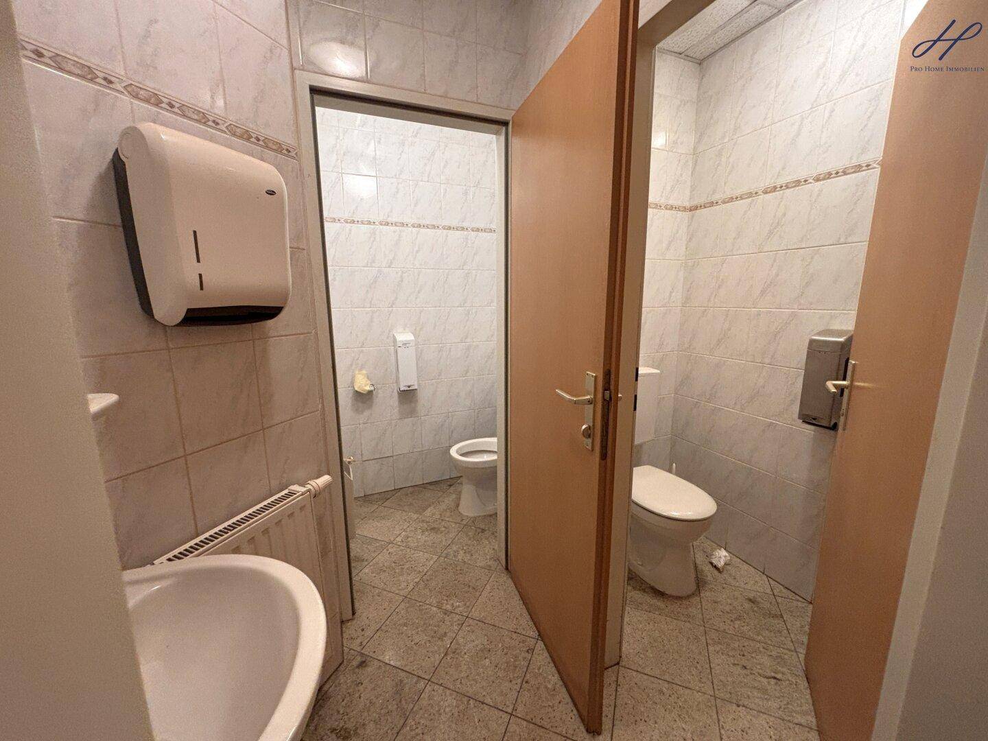 Mehrere Toilettenkabinen in einem öffentlichen Waschraum mit Fliesen an Wänden und Boden.