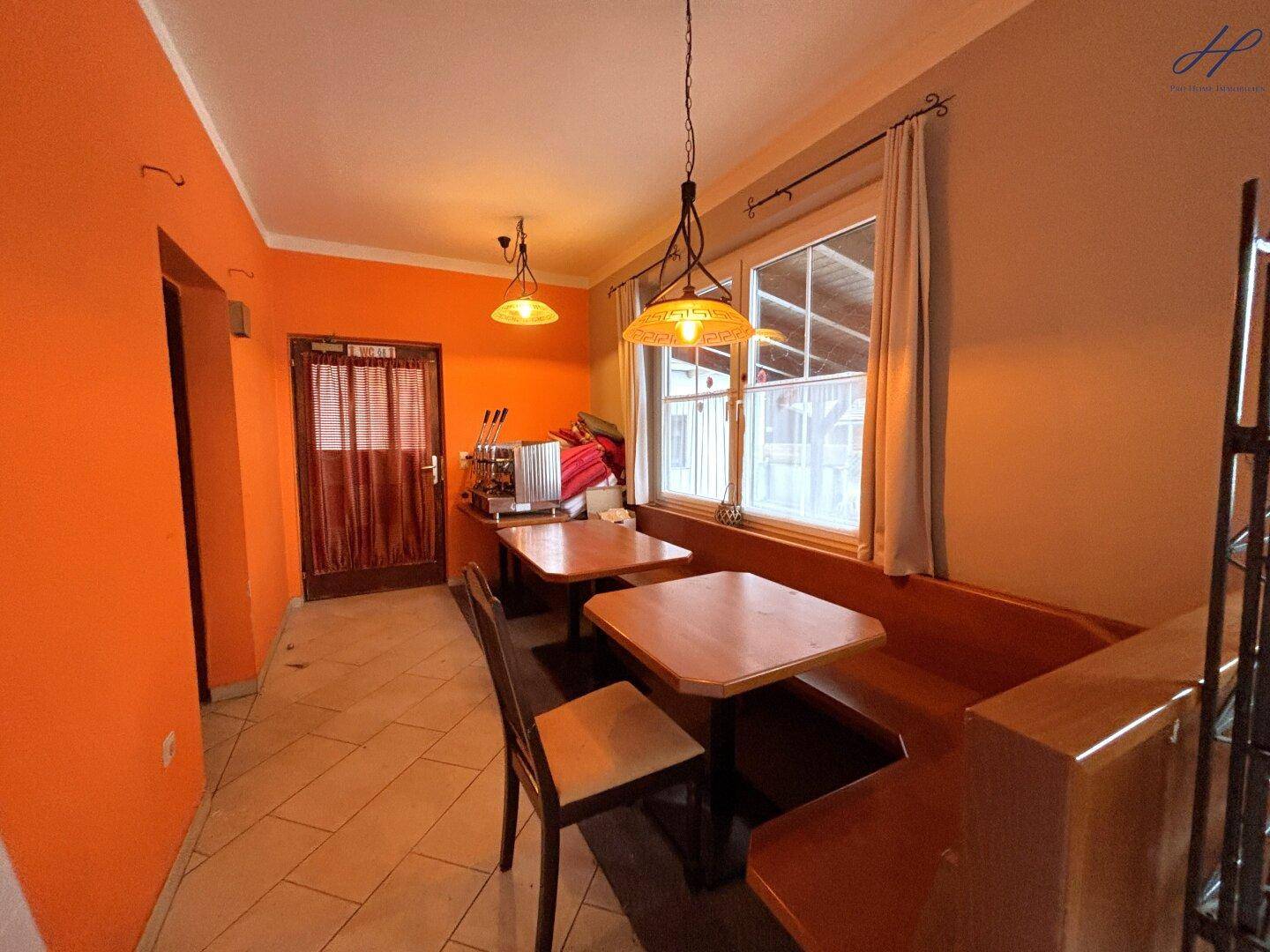 Kleinerer Essbereich mit orangefarbenen Wänden, Holztischen und einer Eckbank, gemütlich und einladend.