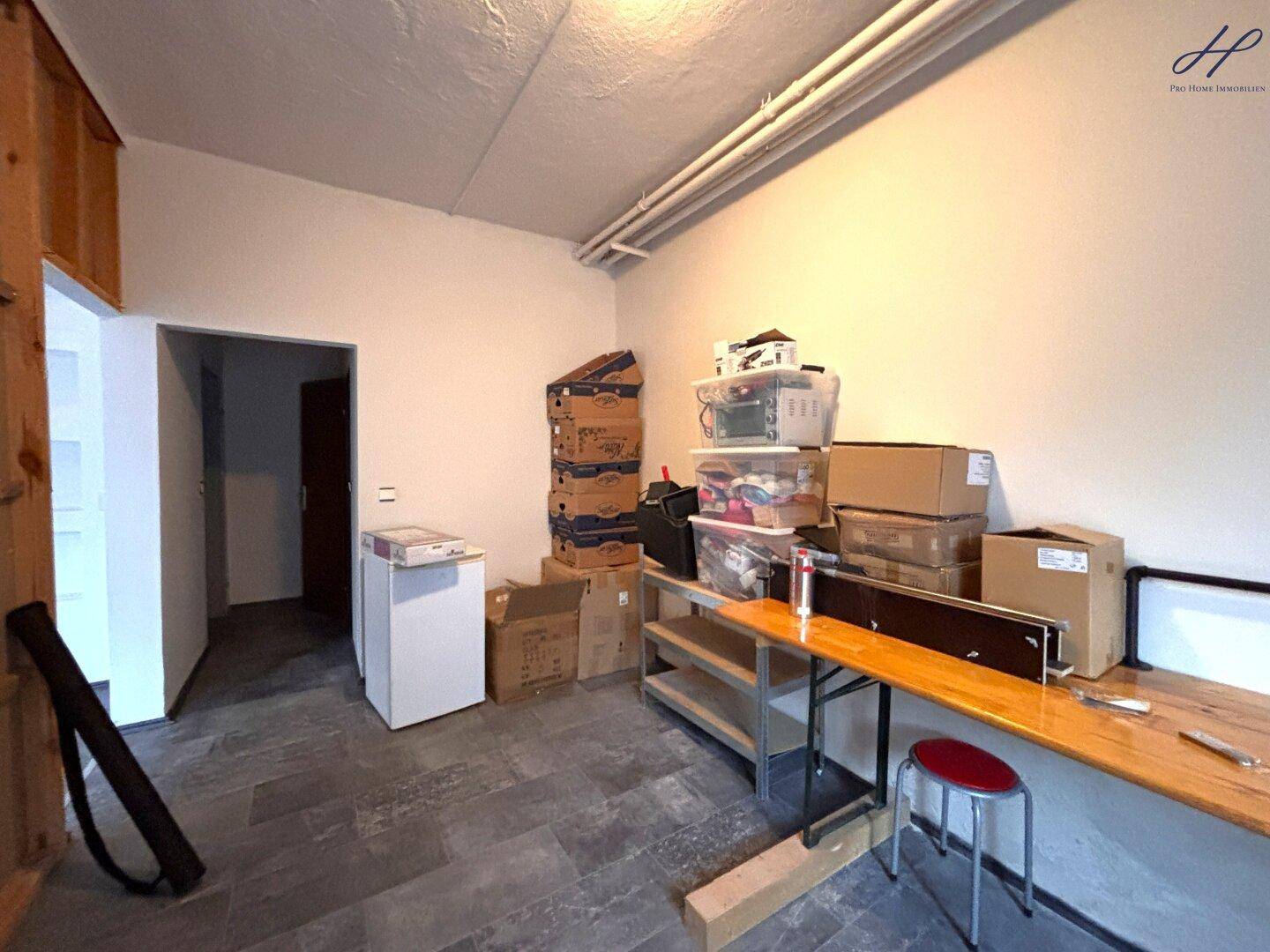 Geräumiger Abstellraum mit Kartons, Regalen und einem kleinen Kühlschrank, bietet viel Stauraum.