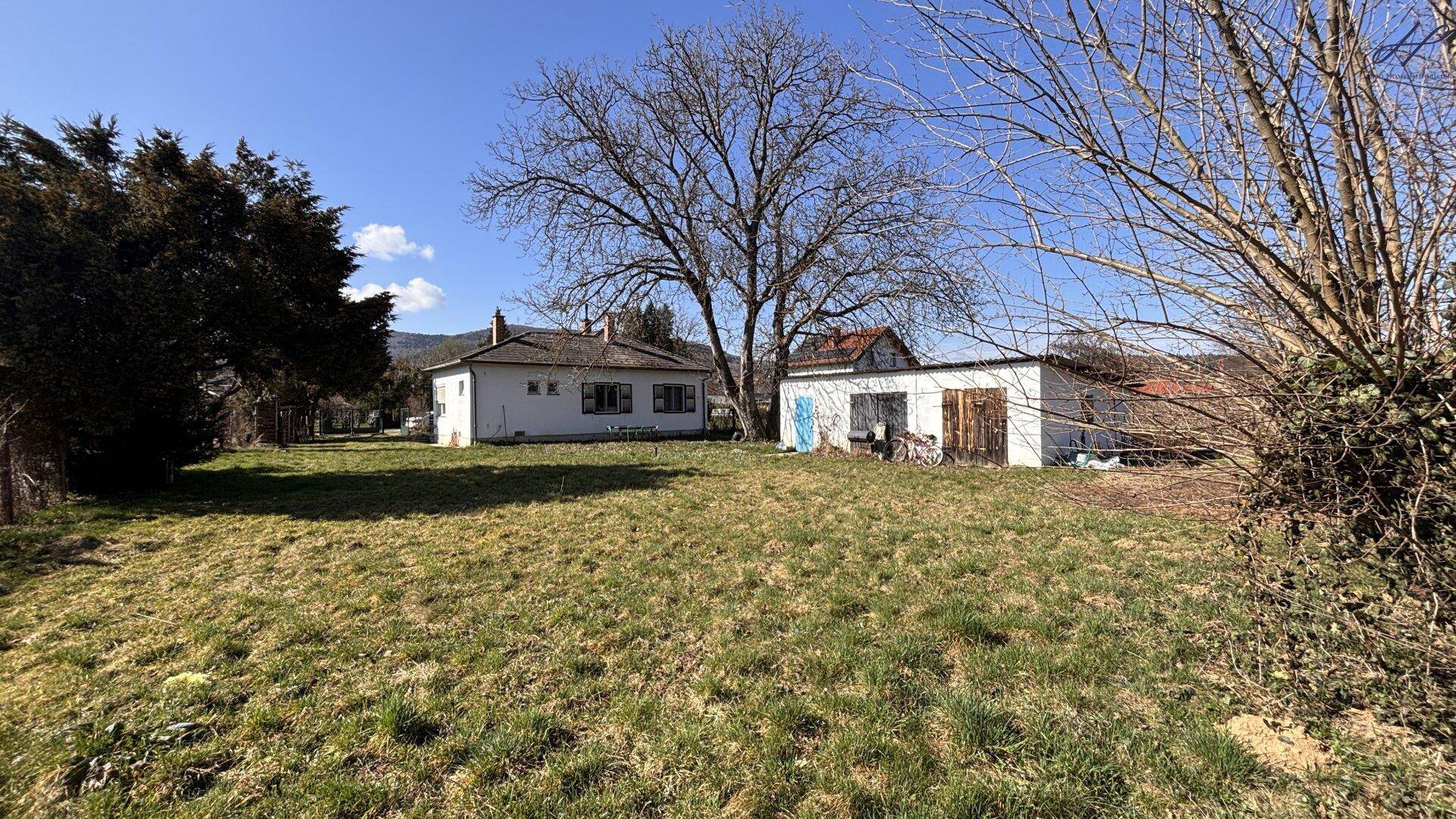 Weitläufiges Grundstück mit Einfamilienhaus und Nebengebäude unter blauem Himmel im Frühling.