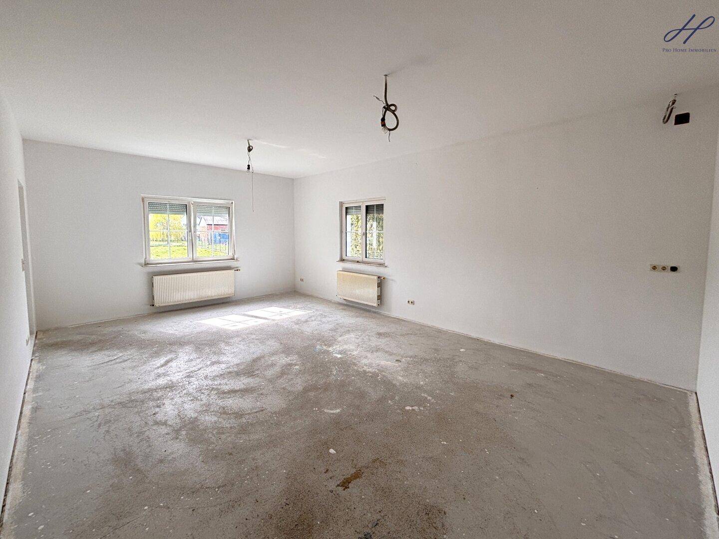 Großes, unmöbliertes Zimmer mit Fenstern und Rohboden, bereit für die Gestaltung.