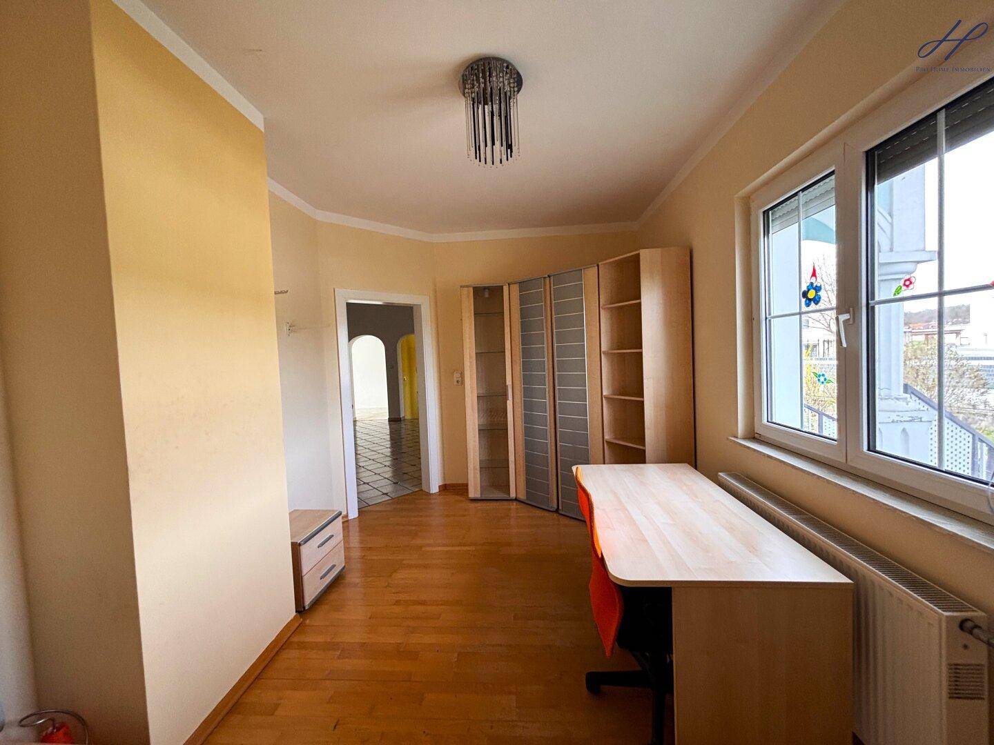 Geräumiges Zimmer mit Holzparkettboden, Fenster und Blick auf den Außenbereich.