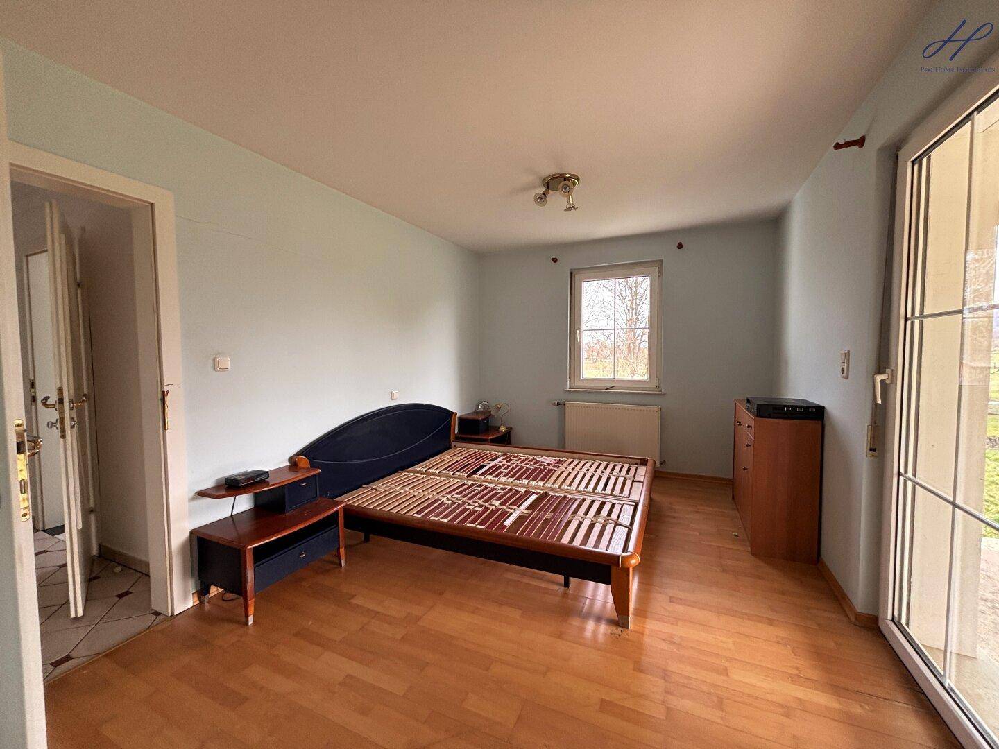 Helles Schlafzimmer mit Holzparkettboden, Bettrahmen und Zugang zur Terrasse.