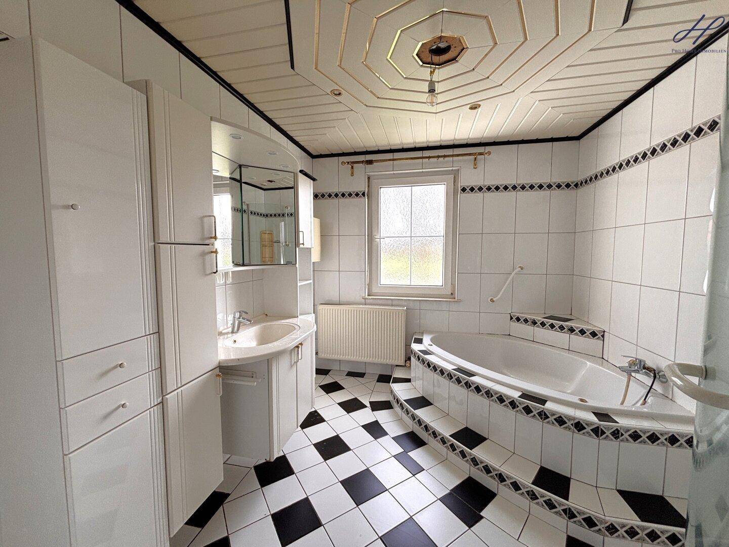 Badezimmer mit schwarz-weißem Fliesenboden, Eckbadewanne und Fenster.