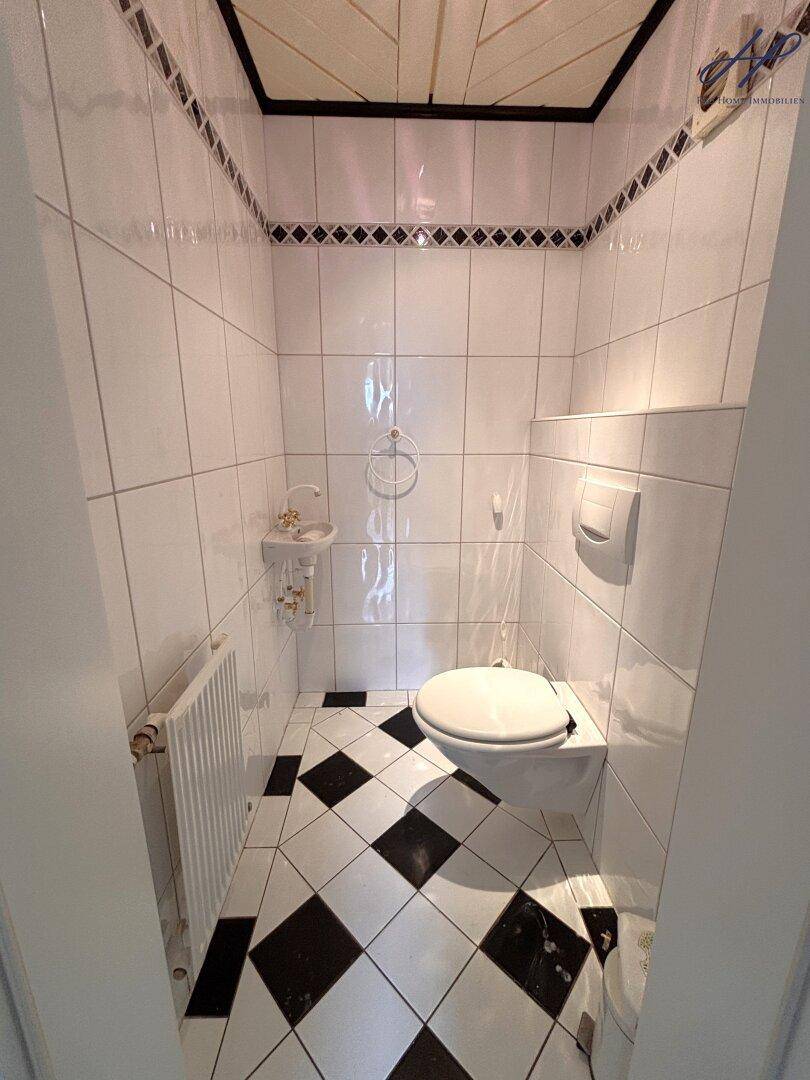 Kleines Gäste-WC mit Wand-WC, Waschbecken und schwarz-weißem Fliesenboden.