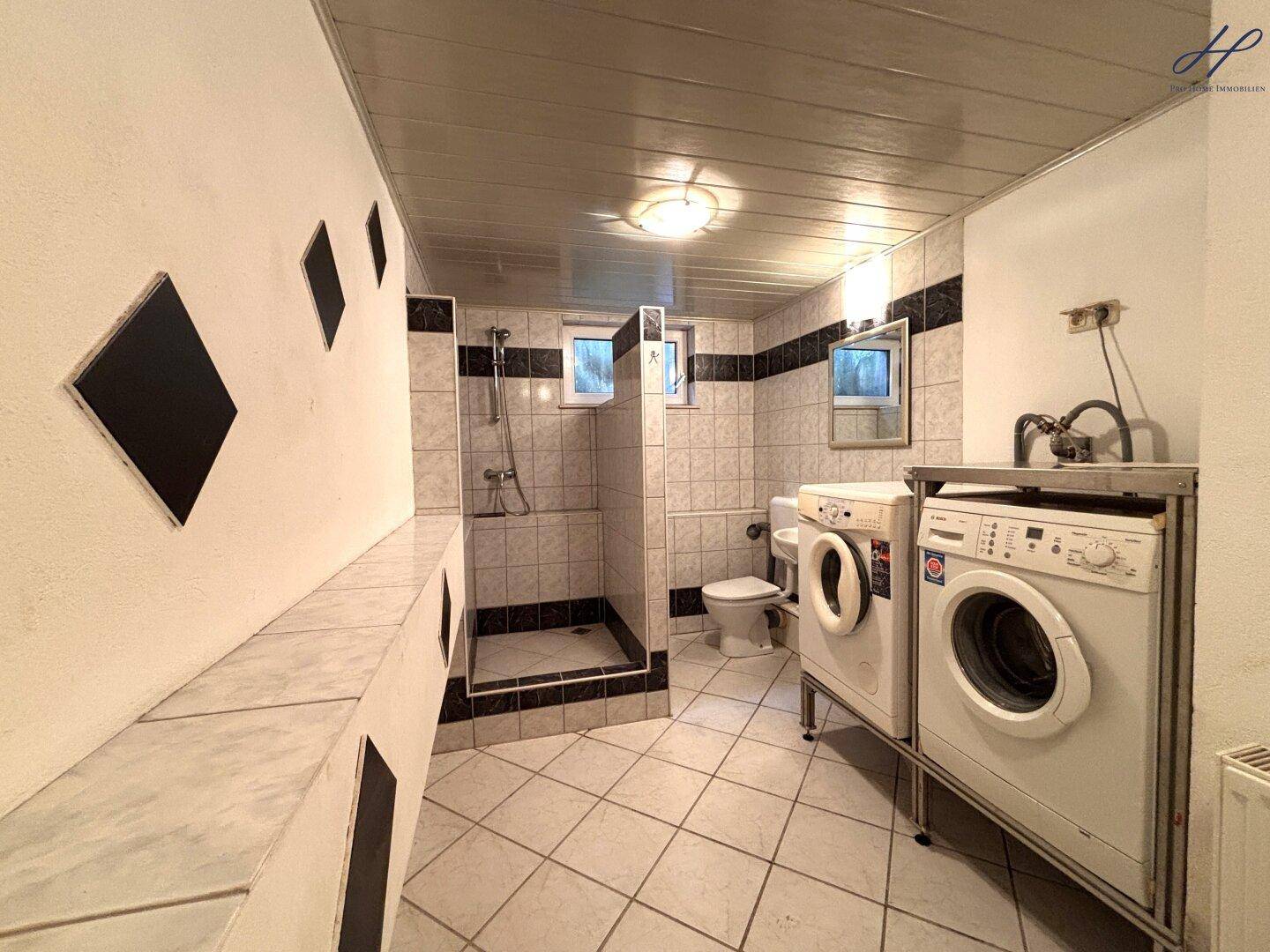 Hauswirtschaftsraum mit Waschmaschine, Trockner, Dusche und Fliesenboden.