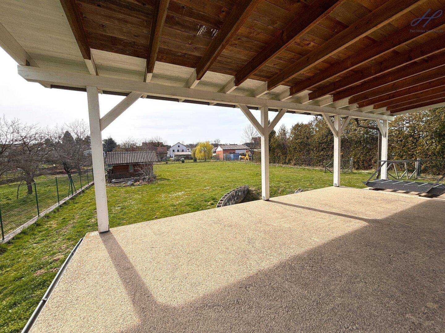 Überdachte Terrasse mit Blick auf den weitläufigen Garten und die ländliche Umgebung, ideal zum Entspannen.