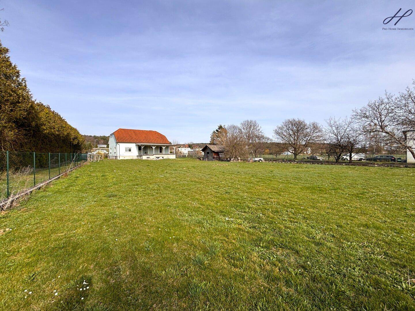 Weitläufige Grünfläche mit einem Einfamilienhaus im Hintergrund und ländlicher Atmosphäre, umgeben von Natur.